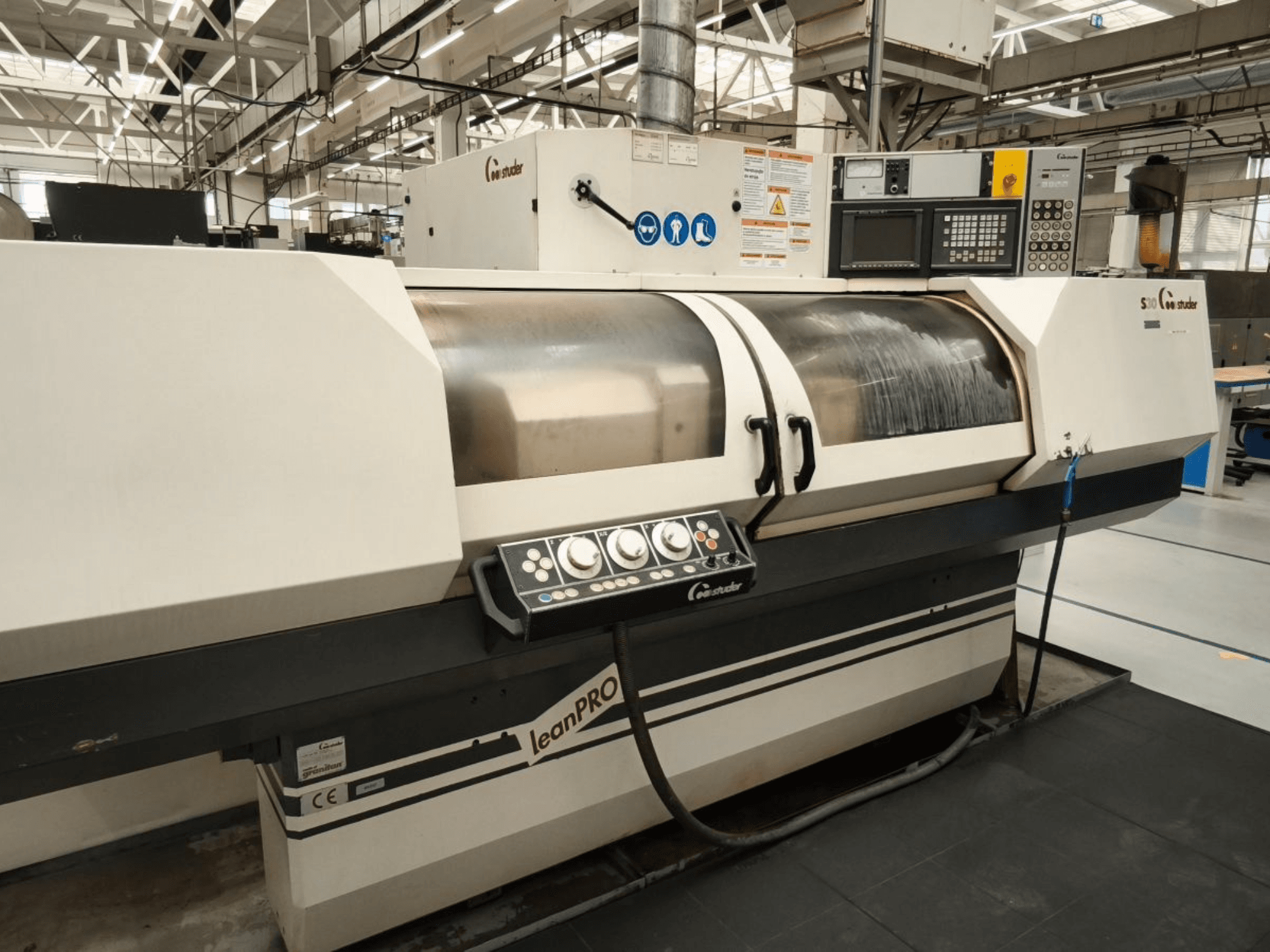 STUDER S30 LEAN PRO cilindriskās slīpmašīnas, skats no sāniem, redzams vadības panelis un slīpripas vāks rūpnieciskā vidē.