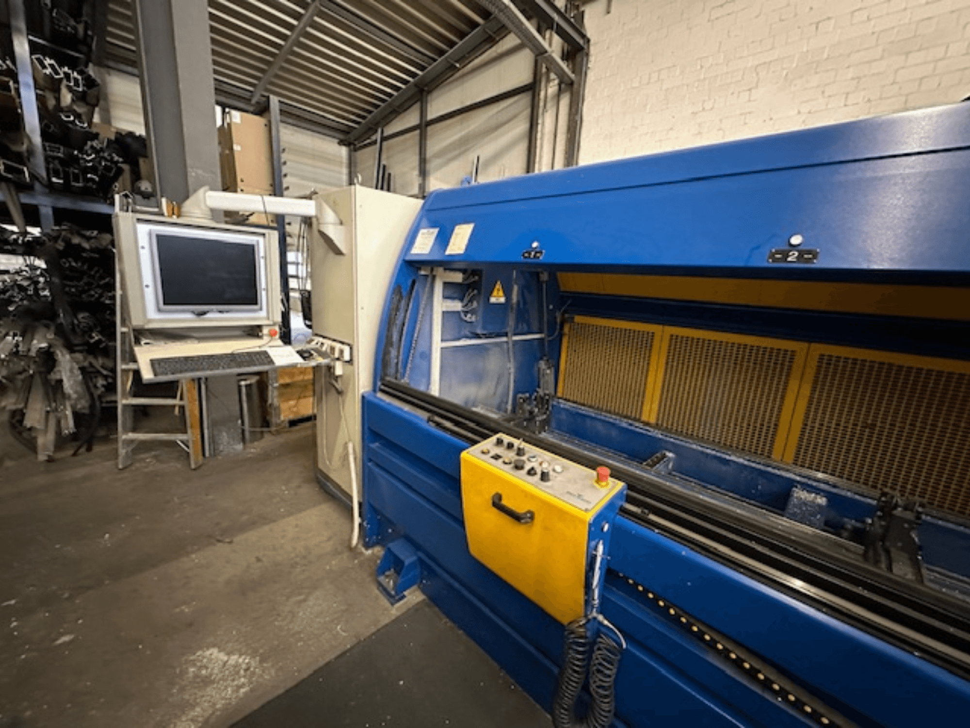 Skats no priekšpuses uz SCHÜCO Profilbearbeitungscenter 299 650, universālo apstrādes centru ar vadības ierīcēm un datora darbstaciju.