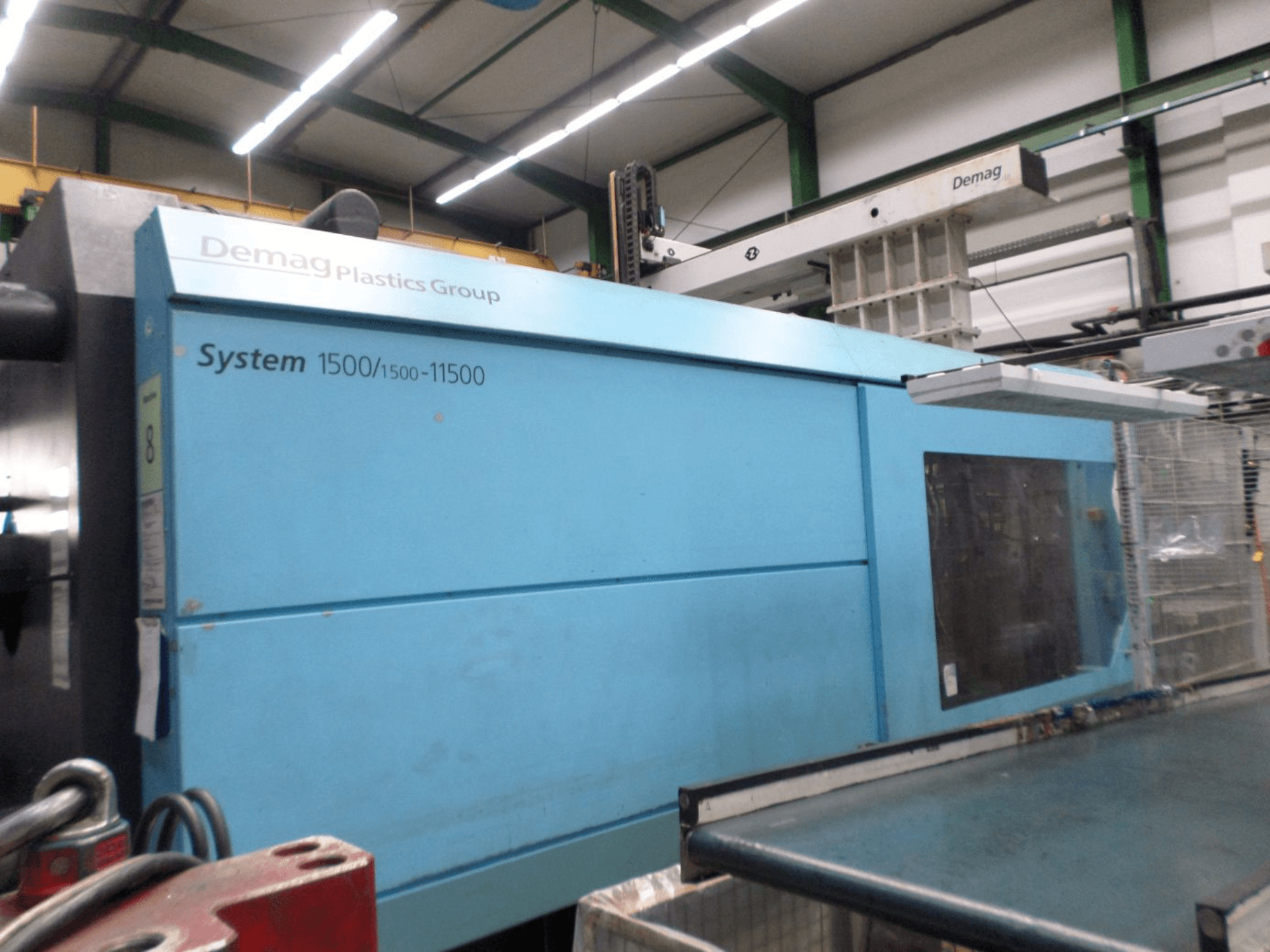 Zilā krāsā izpildīta hidrauliskā plastmasas liešanas mašīna „Demag D 650“ — sānskats, kurā redzams uzraksts „System 1500/1500-11500“ un darba zona.