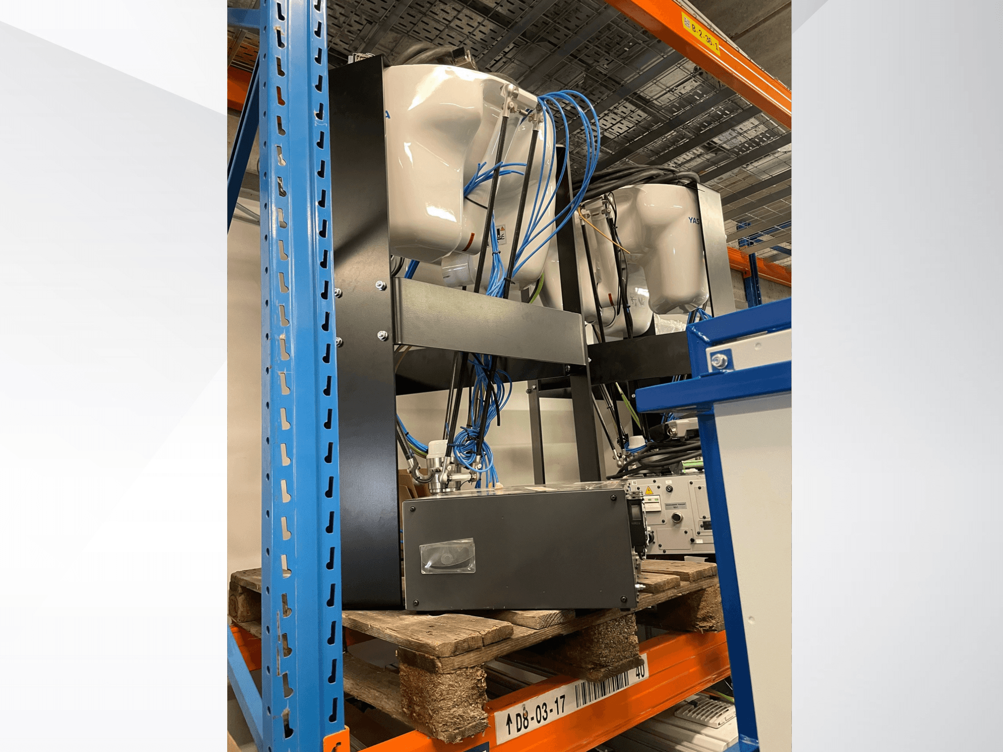 Yaskawa Motoman MPP3H robota roka, redzama no sāniem, ar vadu izvietojumu un komponentiem, kas redzami uz uzglabāšanas plaukta.