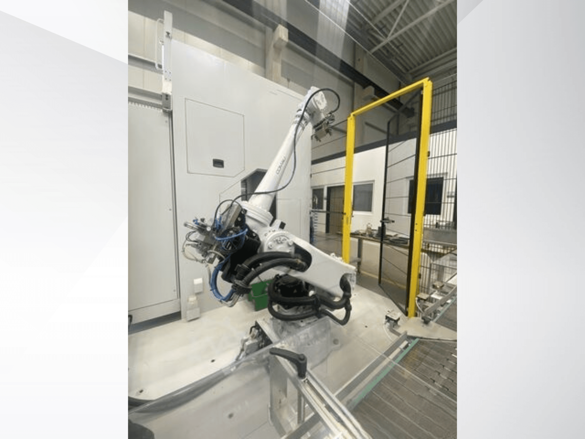 COMAU Smart NJ 40-2.5 robota roka sānu skatā, ar kabeļiem un dzelteniem drošības vārtiem rūpnīcas apstākļos.
