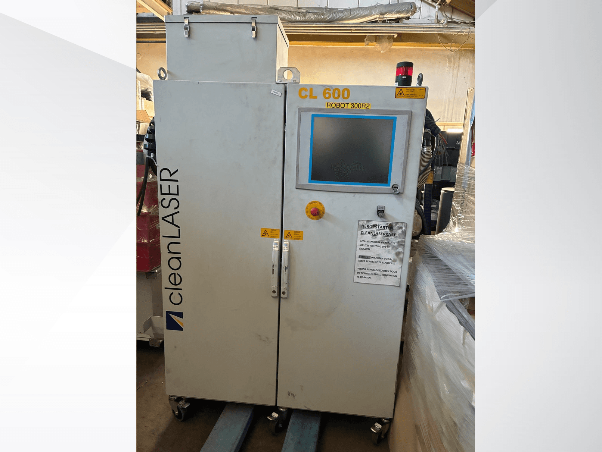 „CLEAN LASER CL 600“ automatizācijas sistēma, skats no priekšpuses, ar LCD displeju, brīdinājuma uzlīmēm un vadības pogām uz durvīm.