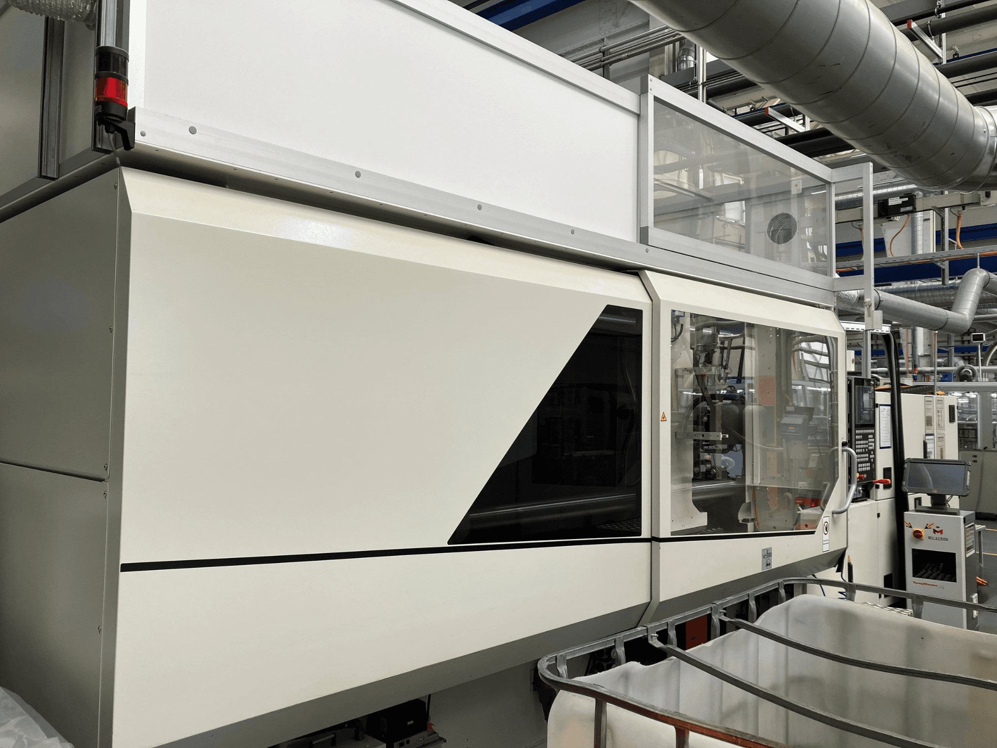 Rūpnieciskās mašīnas priekšējais skats ar gludu baltu dizainu, displeja paneli un stikla sekciju komponentu redzamībai.