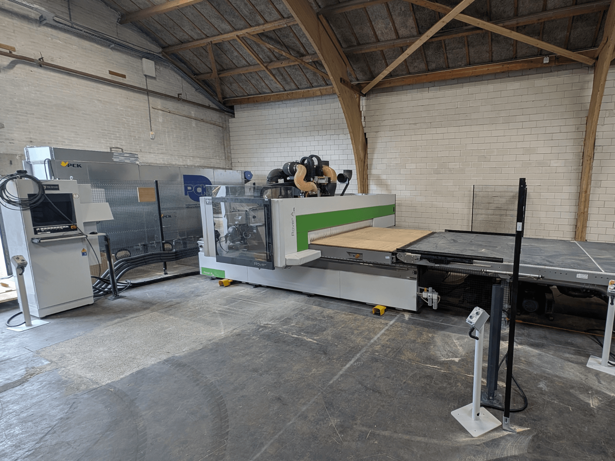 PCK CNC apstrādes centrs, skats no priekšpuses, ar lielu griešanas gultni, vadības paneli, putekļu nosūces sistēmu un izturīgu konstrukciju.