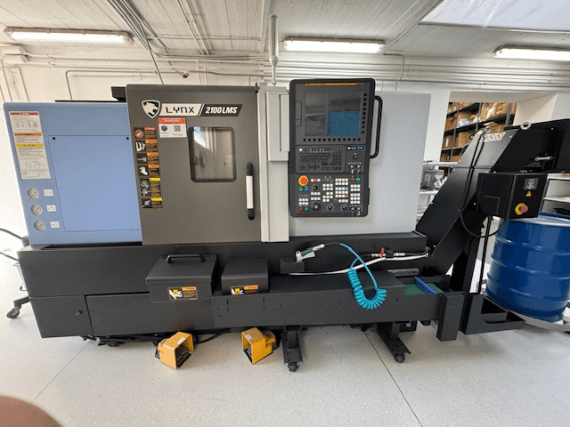 DOOSAN LYNX 2100LMSA horizontālās virpošanas iekārta, skats no priekšpuses, ar vadības paneli, dzesēšanas šķidruma šļūteni un glabāšanas kastēm.