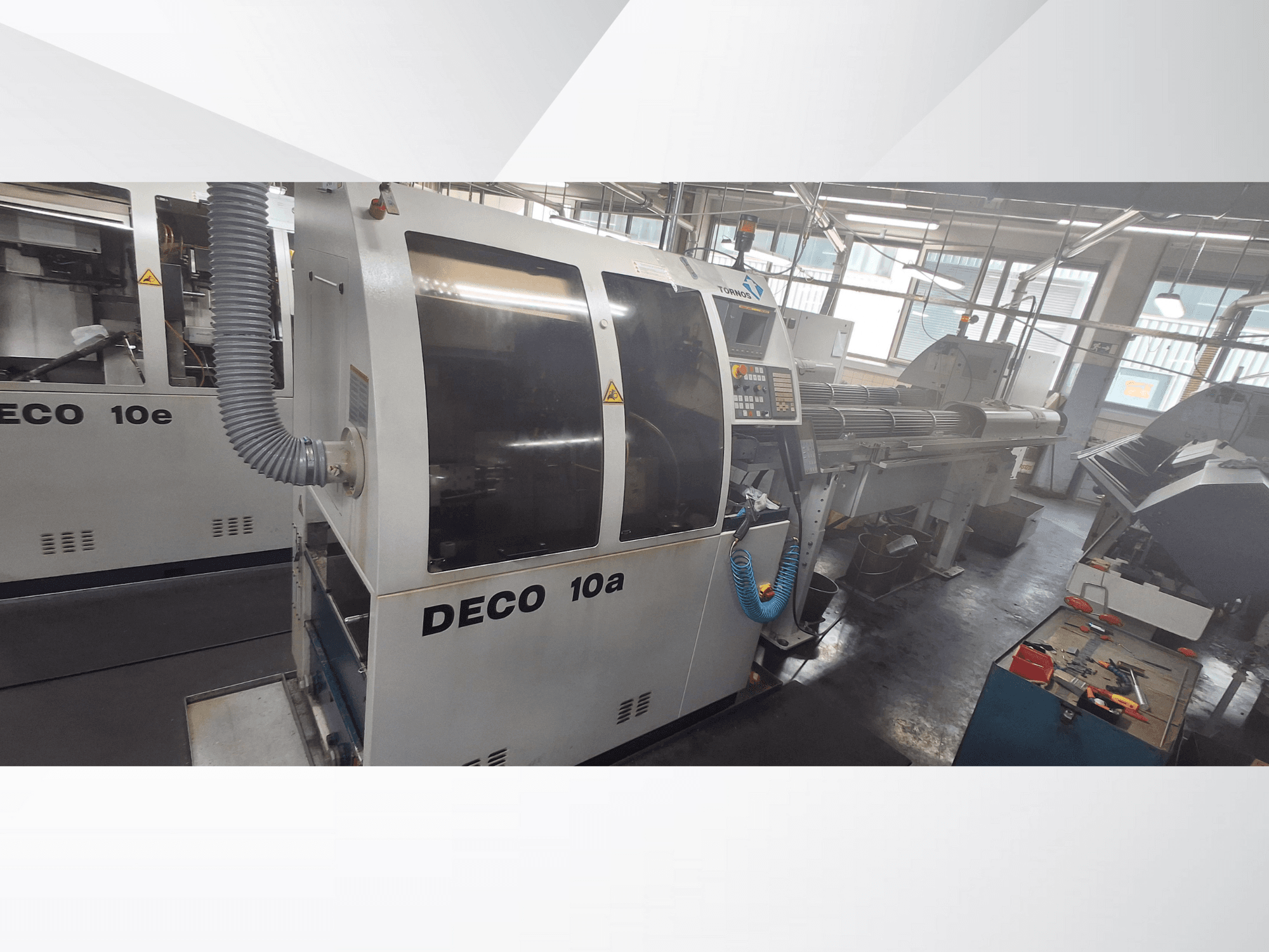 DECO 10a CNC darbnīcā, priekšējais skats, vadības panelis un izplūdes sistēma. Aprīkots ar izturīgu konstrukciju un precīziem instrumentiem.