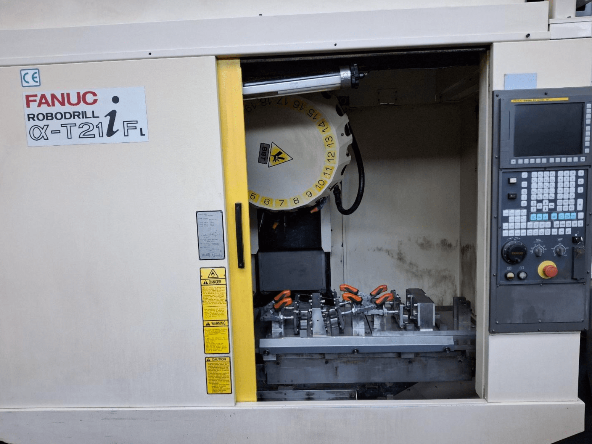 FANUC ROBODRILL α-T21iFL vertikālais apstrādes centrs no priekšpuses, kurā redzami darbgaldi un vadības ierīces mašīnas korpusā.