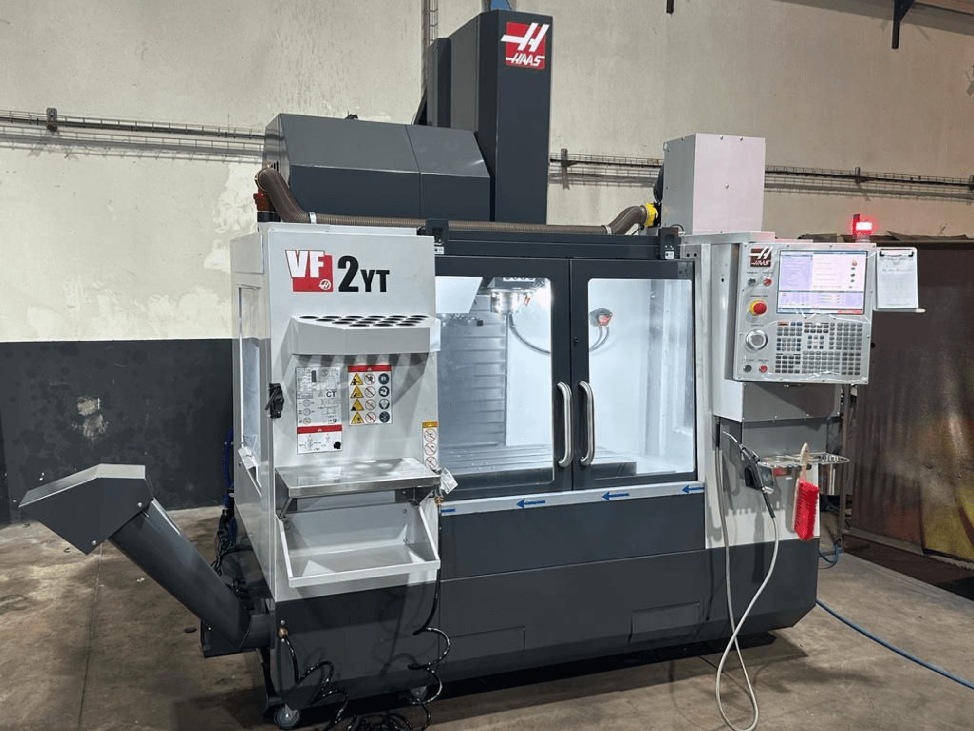 HAAS VF-2YT-EU vertikālais apstrādes centrs, skats no priekšpuses, kurā redzams vadības panelis un instrumentu glabāšanas nodalījums.