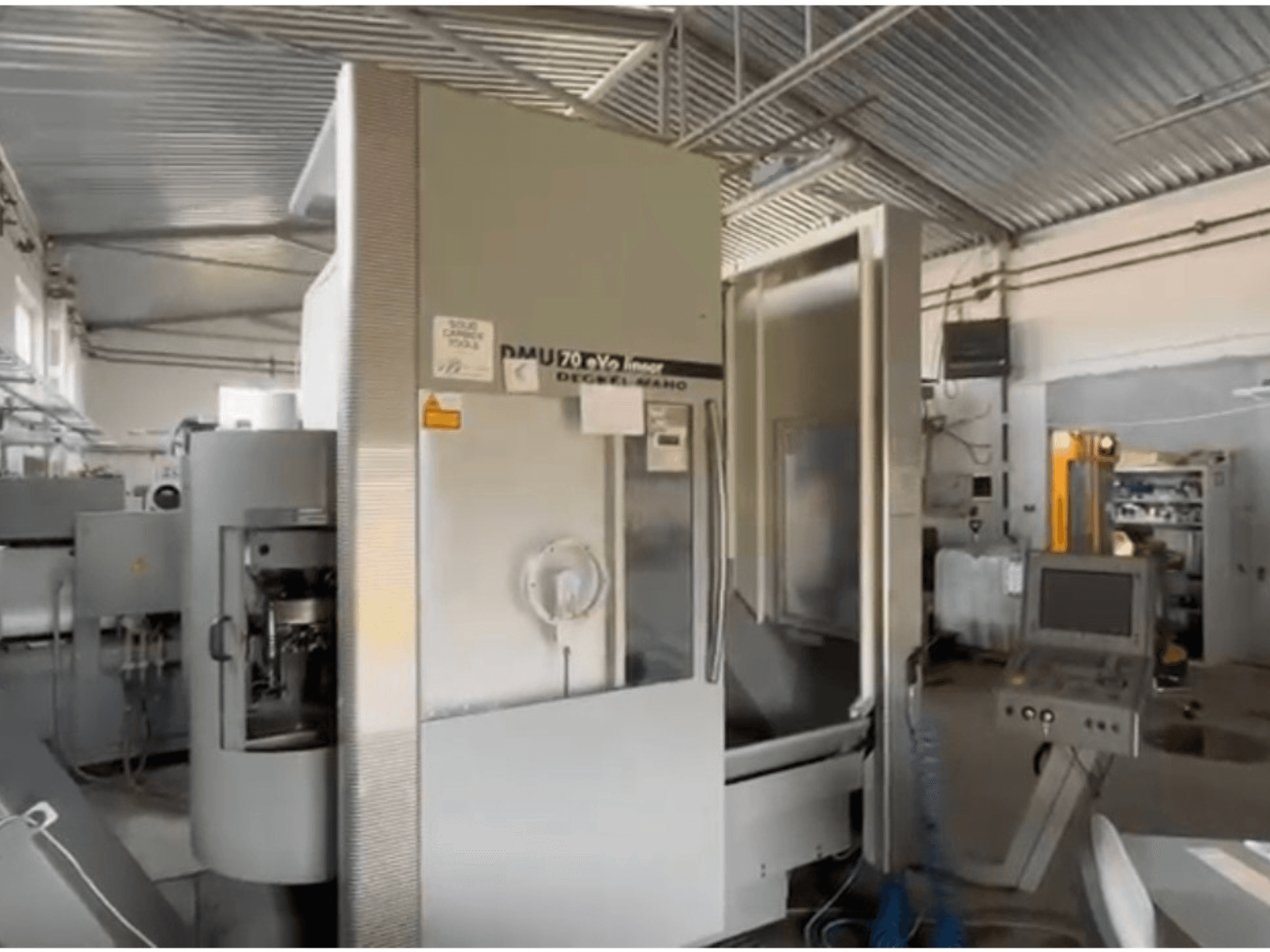 DMU 70 eVo lineārās CNC darbgaldi darbnīcā, skats no priekšpuses, ar vadības paneli un modernu dizainu.