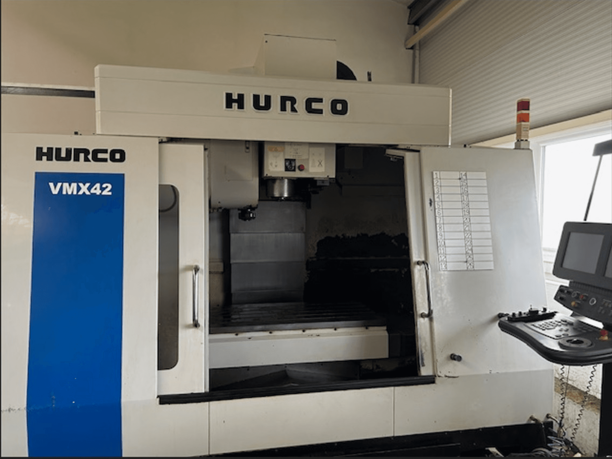 Hurco VMX42 CNC frēzmašīna, skats no priekšpuses, ar vadības paneli un atvērtu darba telpu apstrādes operācijām.