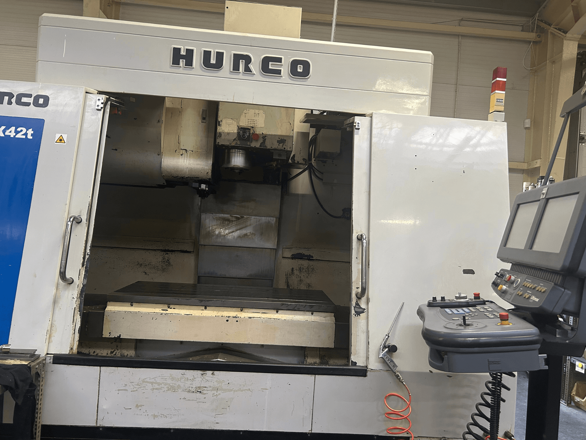 Hurco VMX42T CNC frēzmašīna priekšpusē ar atvērtu darba telpu un vadības paneli ar pogām un displeju.