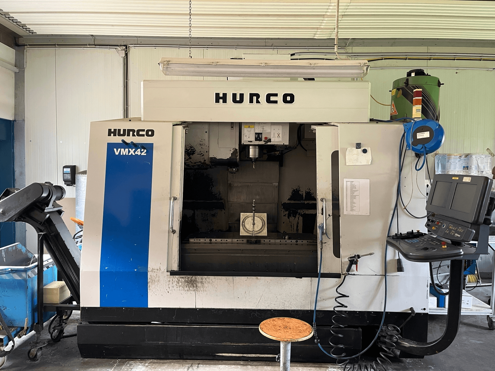 Hurco VMX 42 vertikālais apstrādes centrs sānu skatā, kurā redzams vadības panelis, vārpsta un apstrādājamo detaļu iestatījumi.