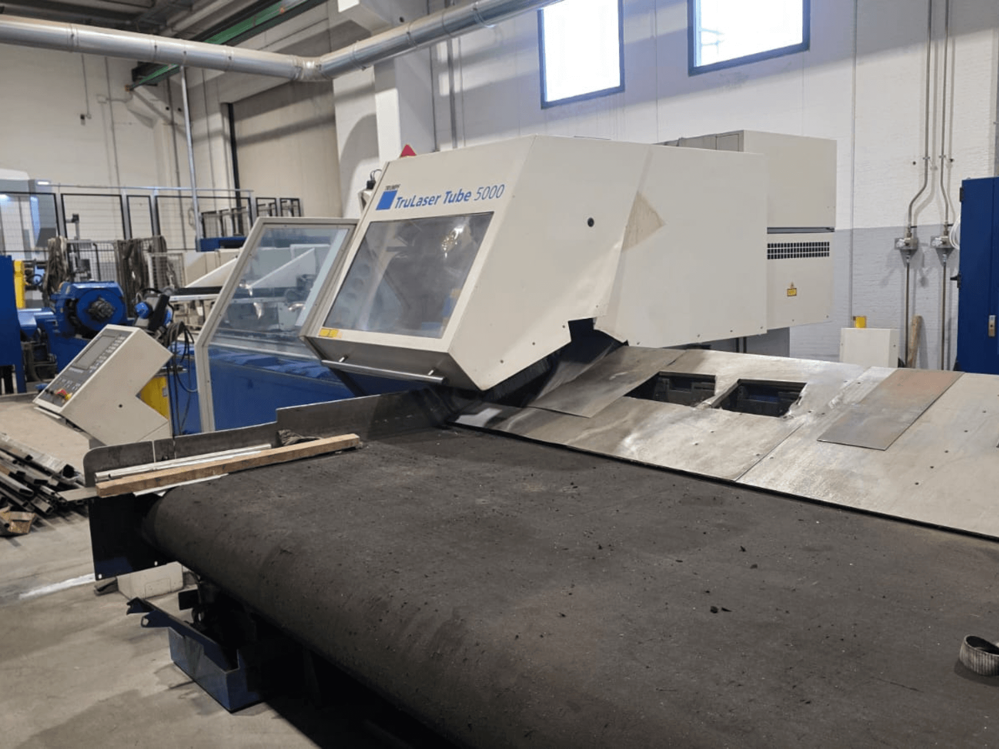 Cauruļu griešanas mašīna TRUMPF LASERTUBE 5000, skats no priekšpuses, kurā redzama griešanas zona un vadības panelis.