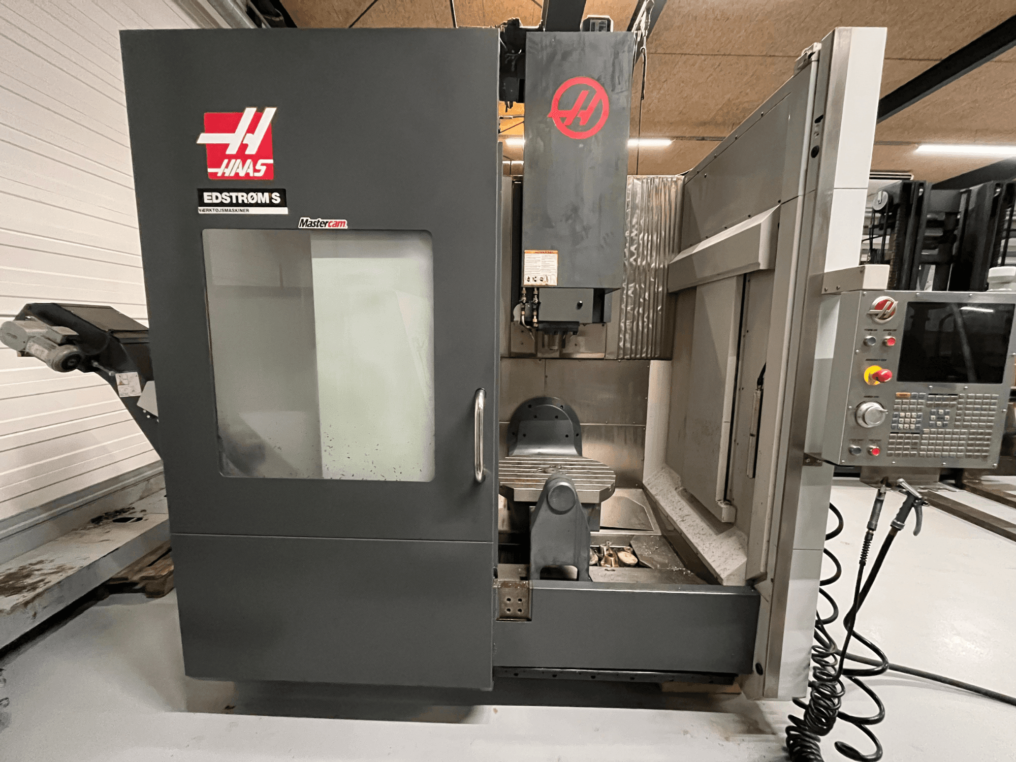 Haas EDSTROM S CNC mašīnas priekšējais skats, kurā redzams vadības panelis, vārpstas galva un apstrādes galds.