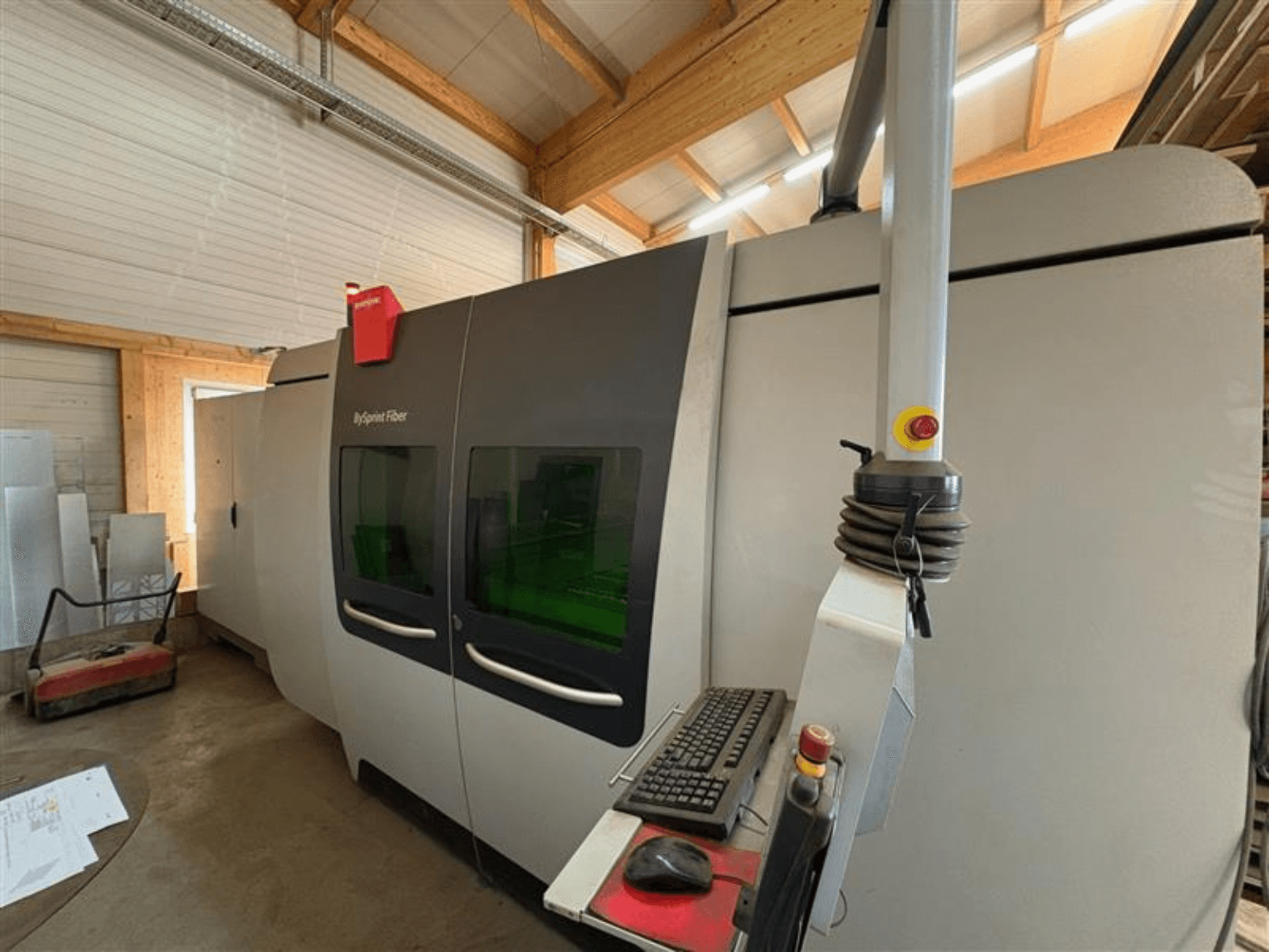 Bystronic ByJet šķiedras griešanas iekārta darbnīcā, priekšējais skats, kurā redzams vadības panelis un divi zaļi skatlogi.