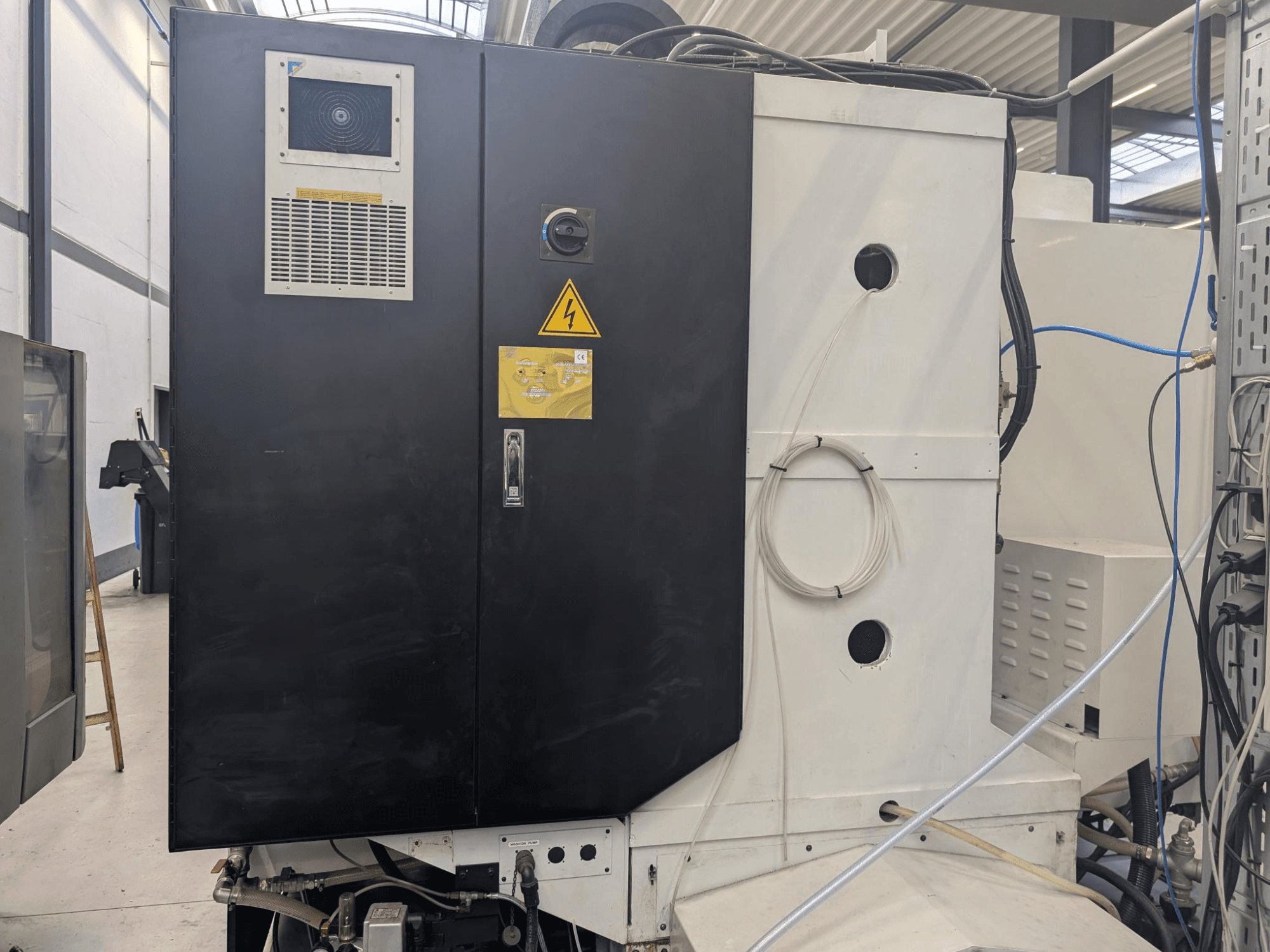 Rūpnieciskas iekārtas melns vadības panelis ar brīdinājuma uzrakstiem, redzamām ventilācijas atverēm un vadiem. Skats no sāniem, kurā redzams dizains un funkcijas.
