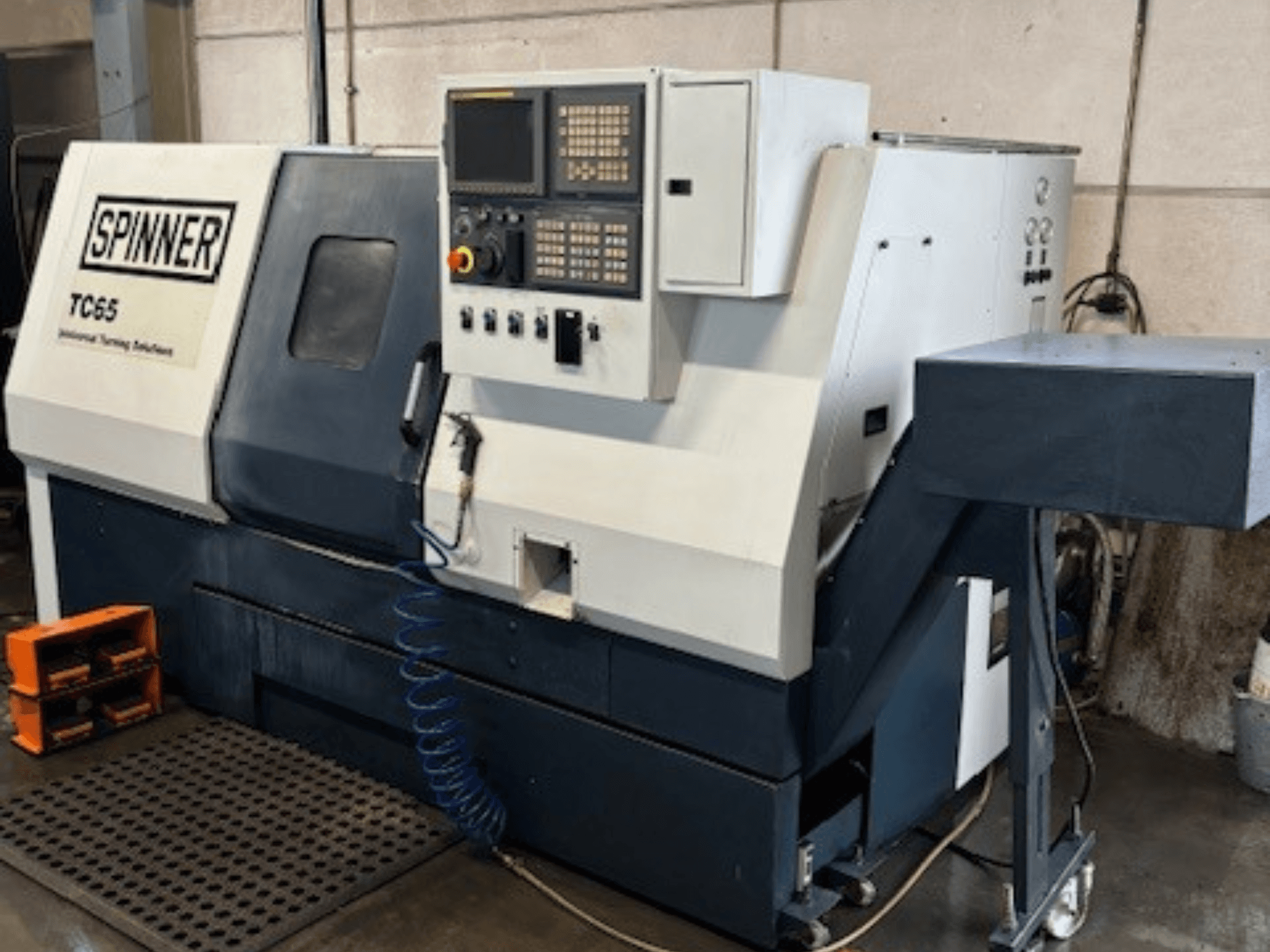 Spinner TC65 rūpnieciskās virpošanas darbgalds, skats no priekšpuses, ar vadības paneli, saspiestā gaisa padeves līniju un instrumentu glabāšanas vietu.