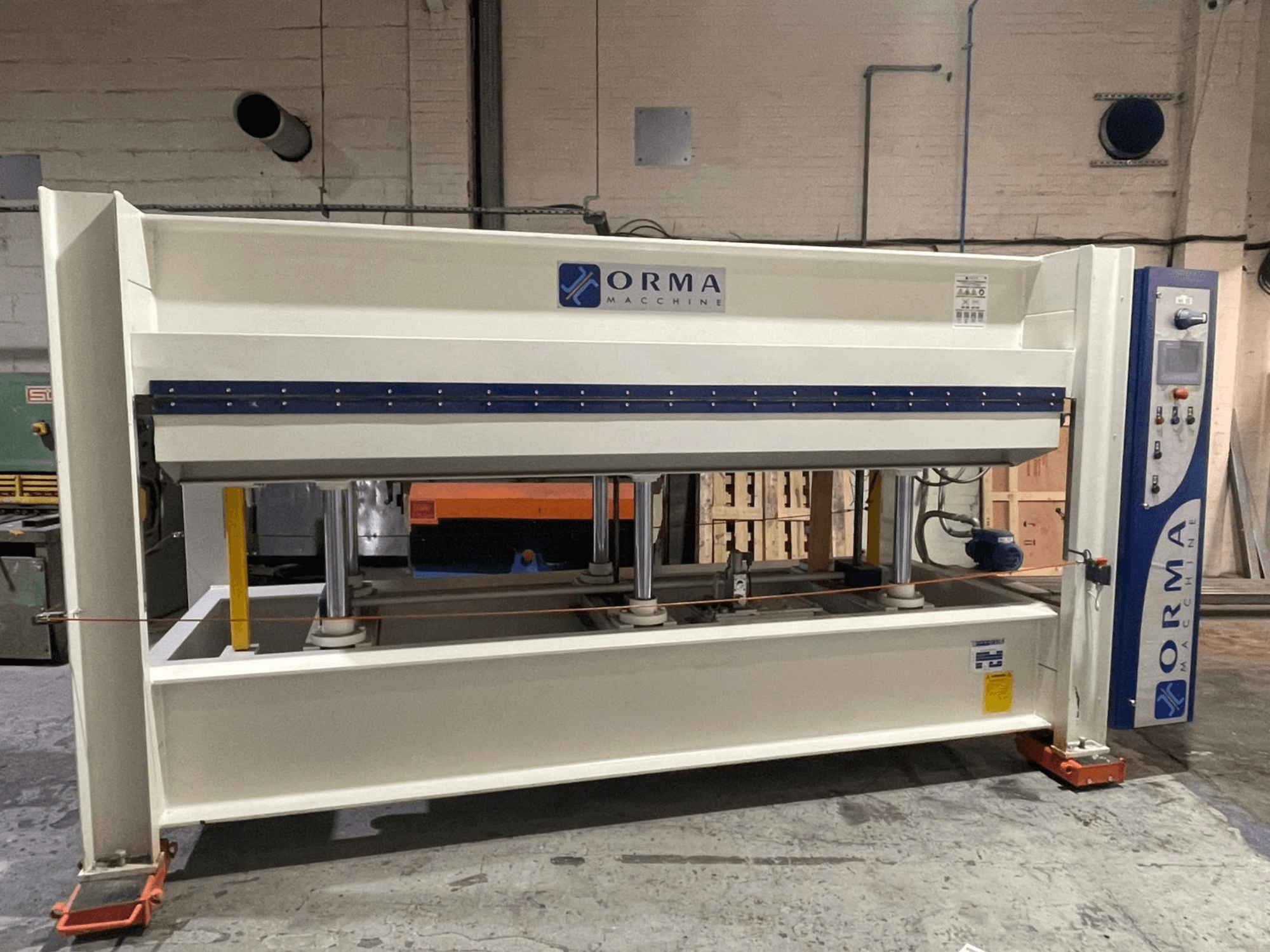 Hidrauliskā prese ORMA machinery, skats no priekšpuses, ar sudraba apdari, vadības paneli labajā pusē un vertikāliem presēšanas virzuļiem.