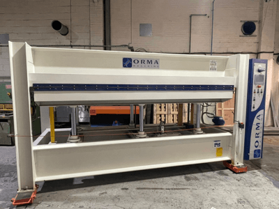 Hidrauliskā prese ORMA machinery, skats no priekšpuses, ar sudraba apdari, vadības paneli labajā pusē un vertikāliem presēšanas virzuļiem.