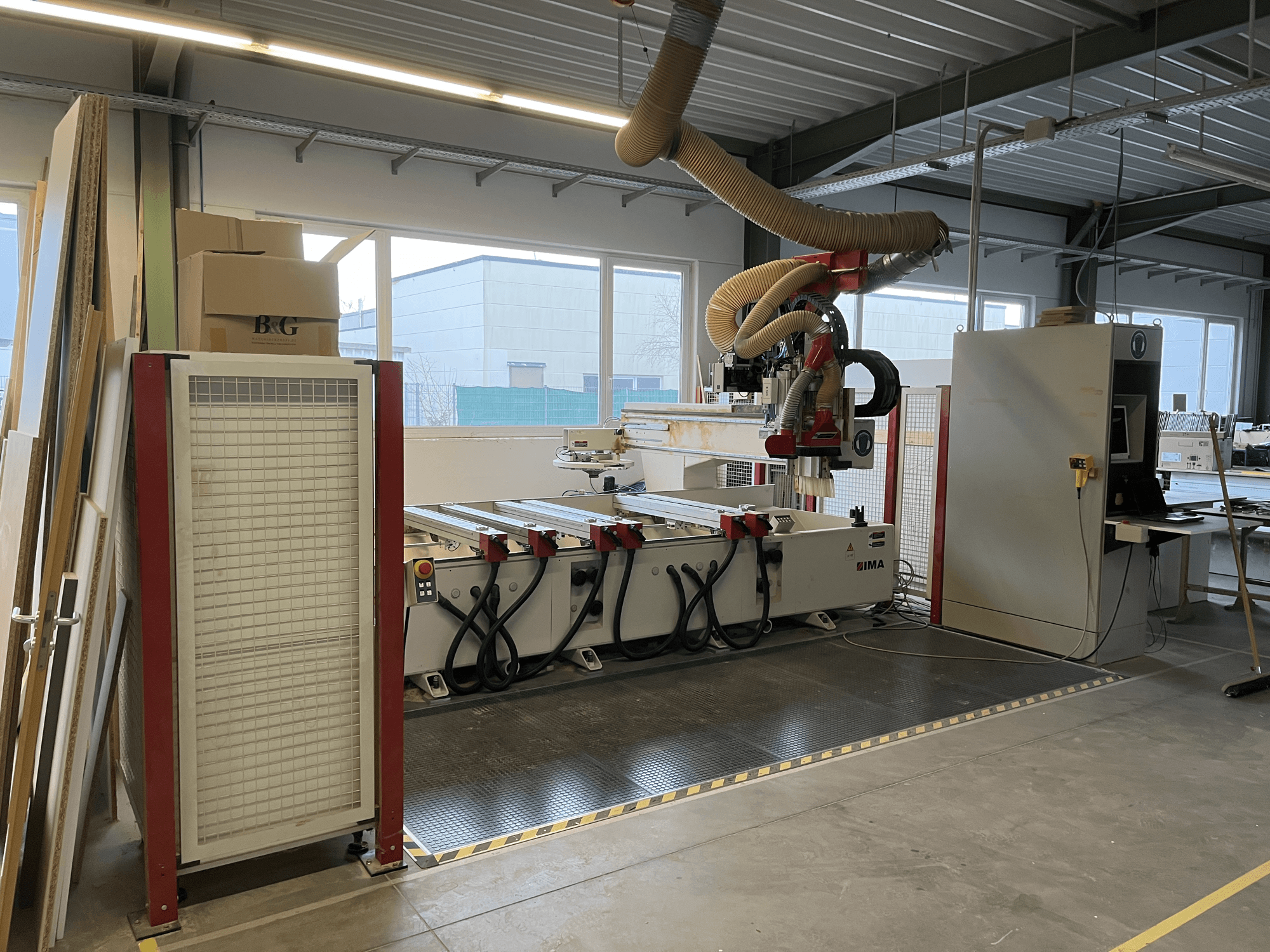 CNC kokapstrādes centrs IMA BIMA 410 darbnīcā, skats no sāniem, redzams vadības panelis un putekļu nosūces sistēma.