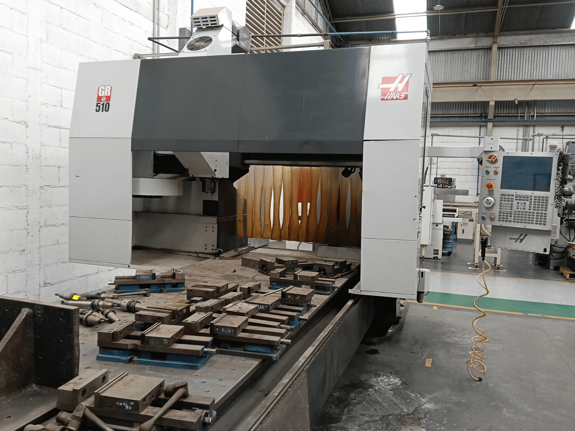 HAAS GR-510 portālfrēzēšanas stenda skats no priekšpuses, kurā redzams vadības panelis un apstrādātie detaļas uz galda.