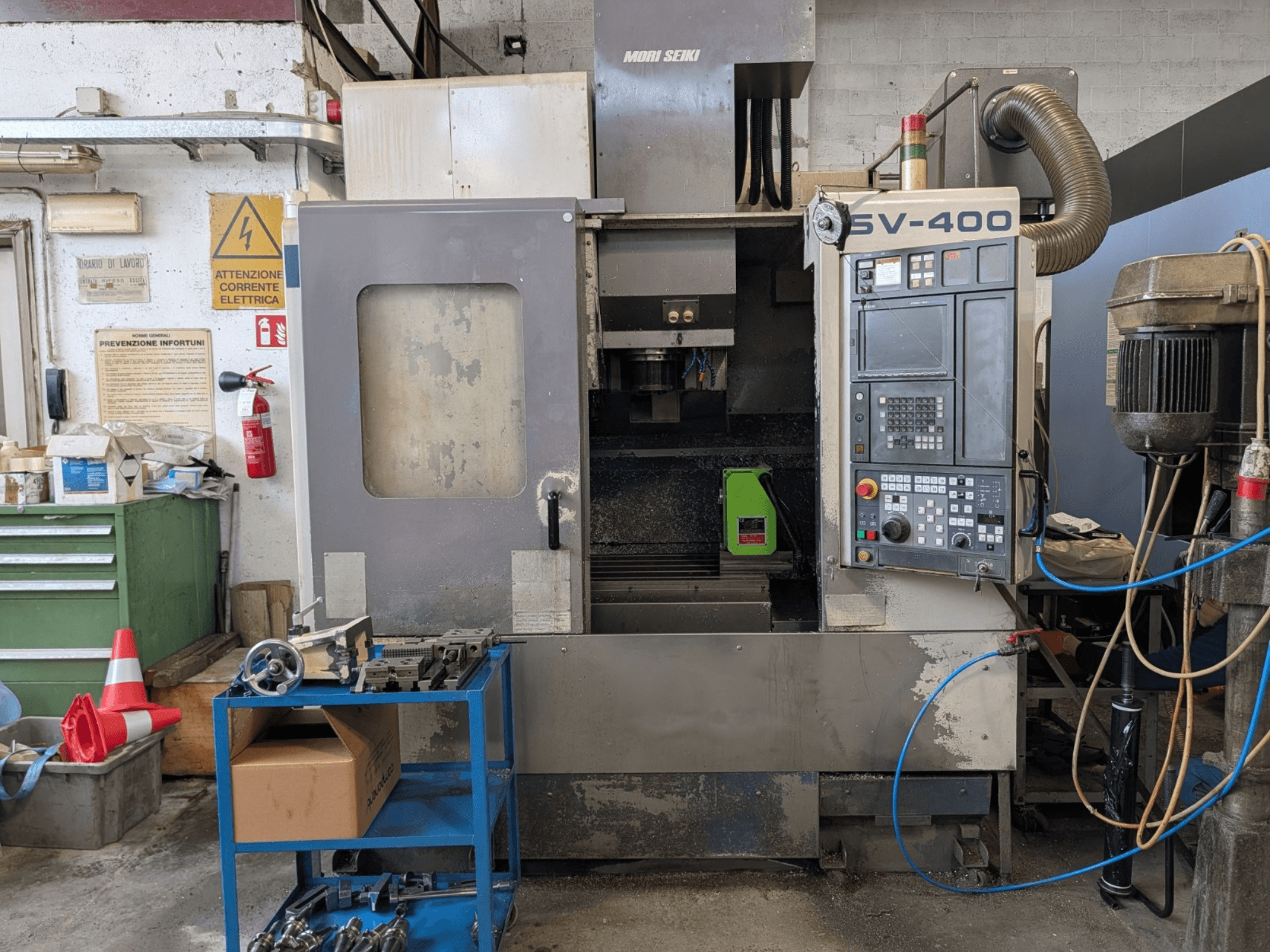 MORI SEIKI SV-400 vertikālais apstrādes centrs darbnīcā, skats no sāniem, blakus redzams vadības panelis un darbgaldi.