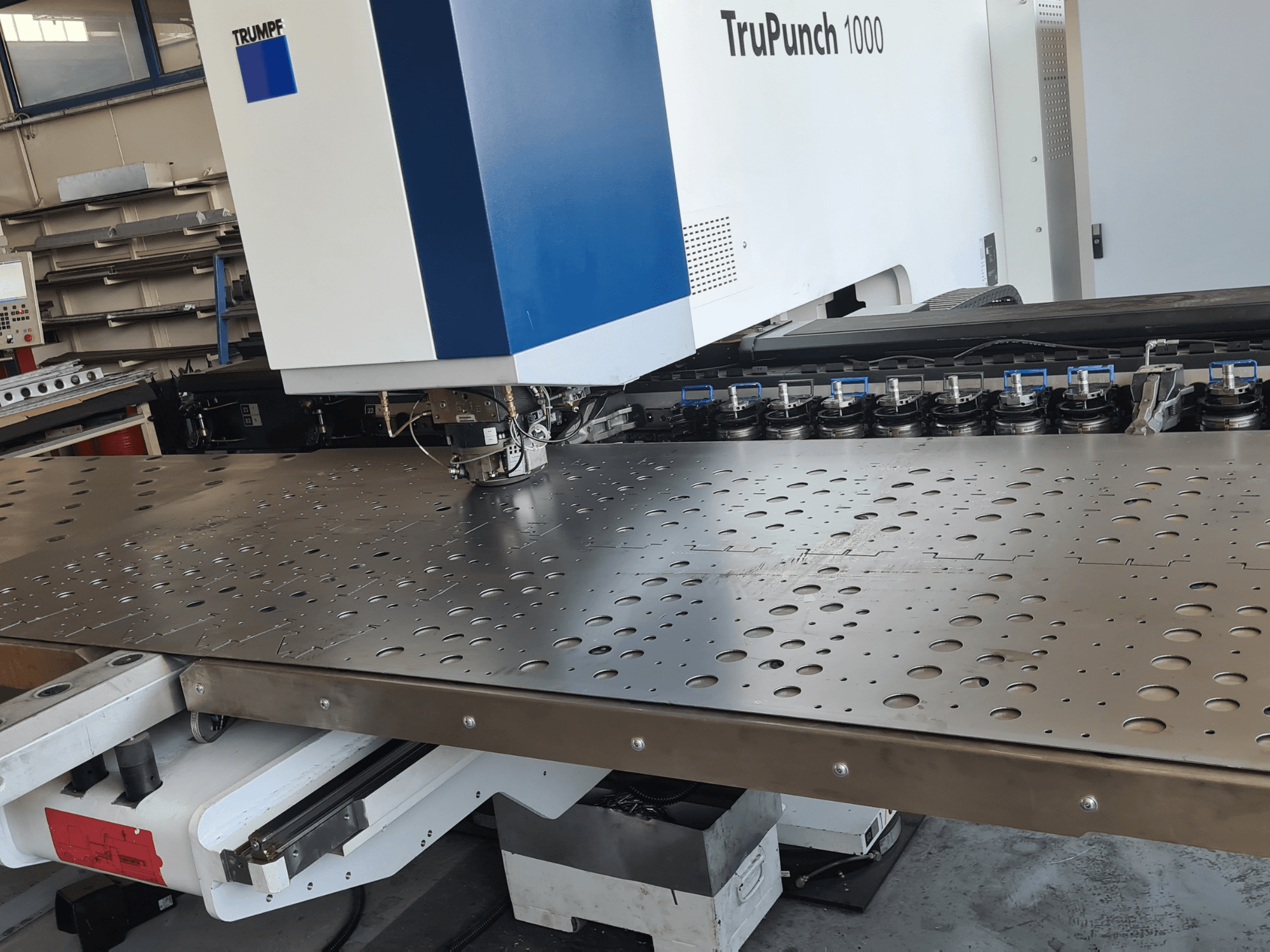 CNC perforācijas stends TRUMPF TruPunch 1000, skats no priekšpuses, kurā redzama perforēta metāla loksne un instrumentu uzstādījums.