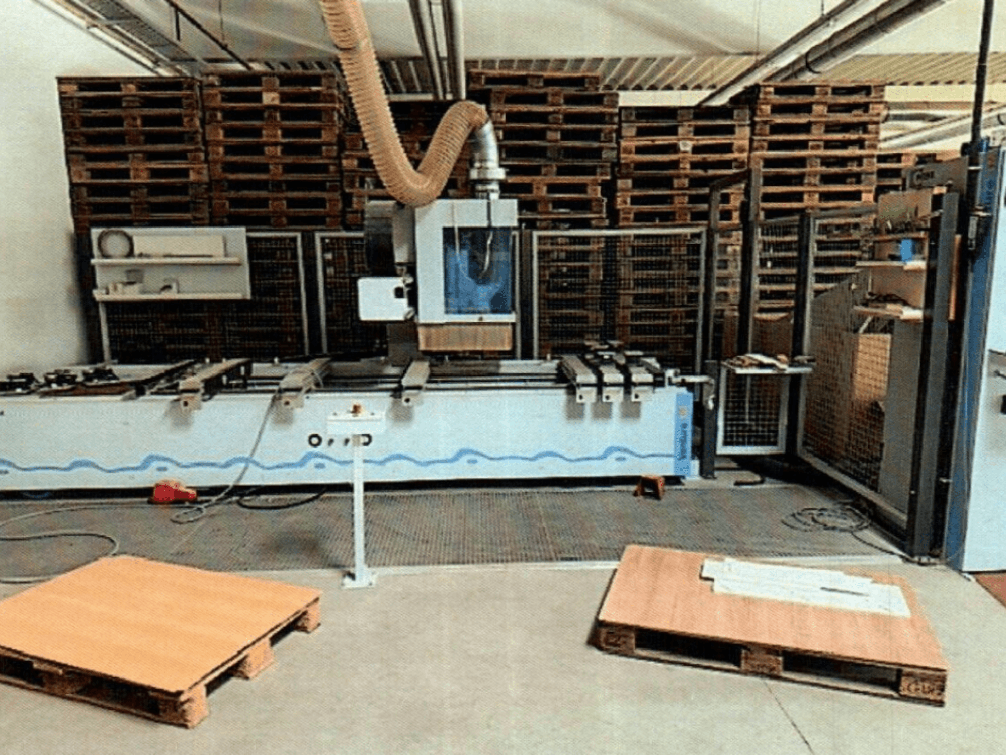 CNC kokapstrādes centrs Weeke Venture 1M darbnīcā, skats no priekšpuses ar redzamiem koka paliktņiem un rūpniecisko uzstādījumu.