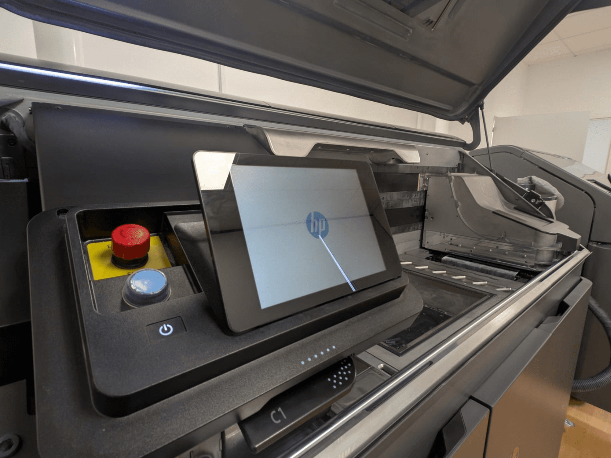 HP printera vadības panelis, kurā redzams planšetdatora displejs, sarkanās un zilās pogas, kā arī skats uz printera iekšējām sastāvdaļām no sāniem.