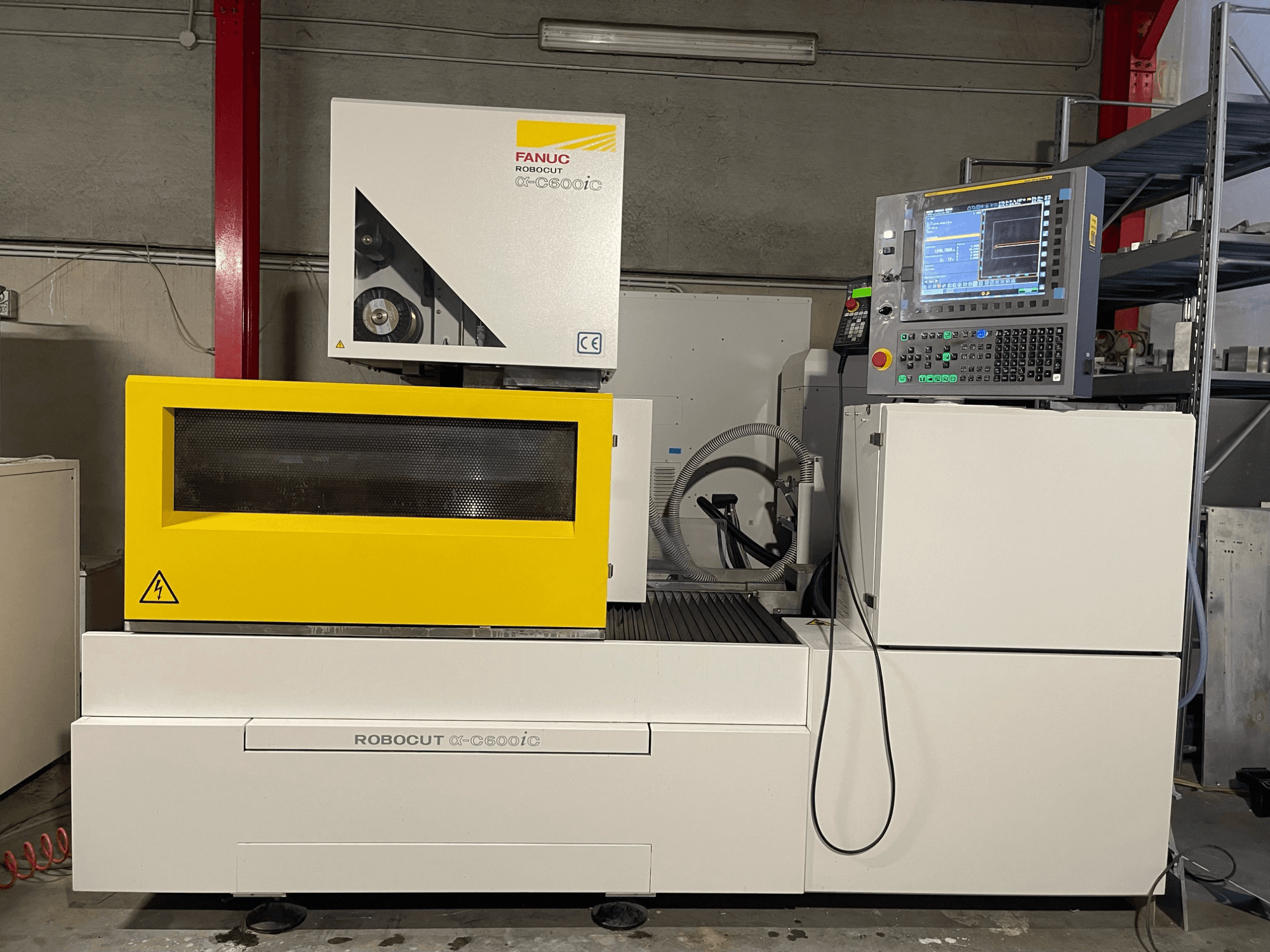 FANUC Robocut α-C600iC, skats no sāniem uz CNC mašīnu ar dzeltenu drošības vāku un vadības paneli, kas demonstrē precīzas griešanas iespējas.