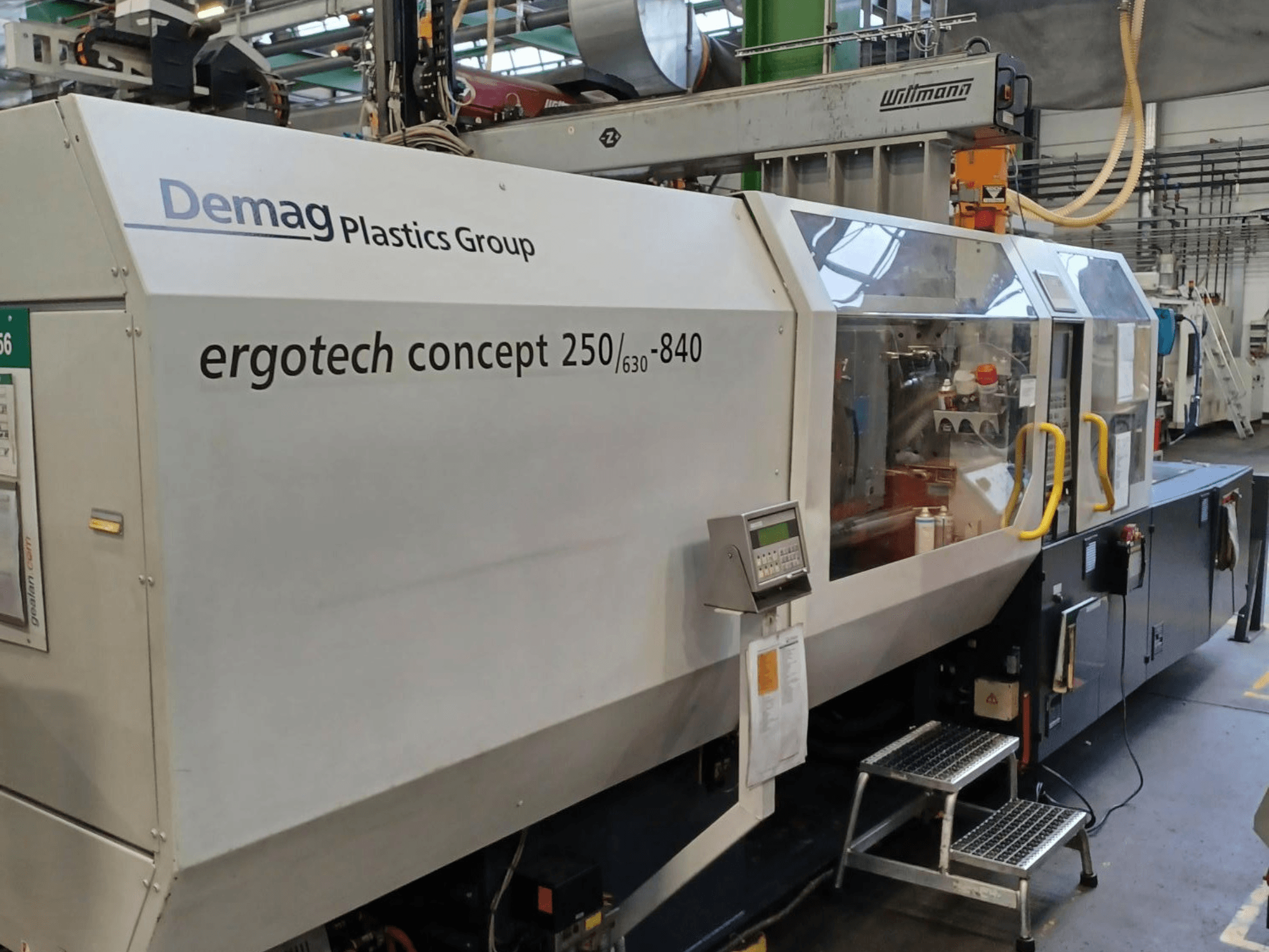 Demag ergotech concept 250/630-840 iesmidzināšanas mašīna, skats no priekšpuses, redzamas digitālās vadības ierīces un caurspīdīgie drošības pārsegi.