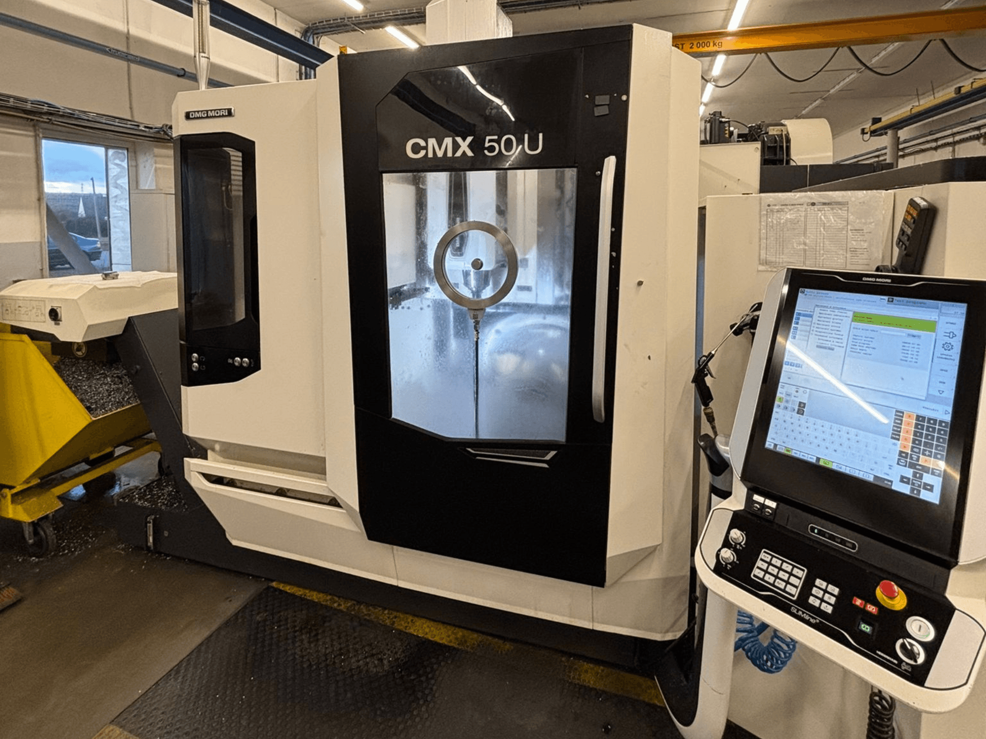 DMG MORI CMX 50 U vertikālais apstrādes centrs, priekšējais skats ar vadības paneli un stikla displeju, kurā redzama iekšējā mehānika.