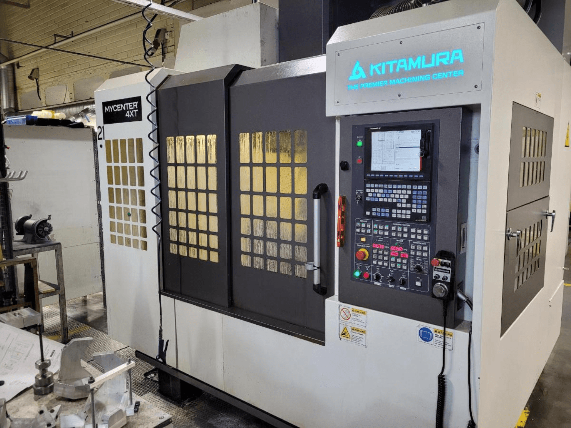 Kitamura Mycenter-4XT apstrādes centra vertikālais skats ar vadības paneli un izgaismotu zīmolu.