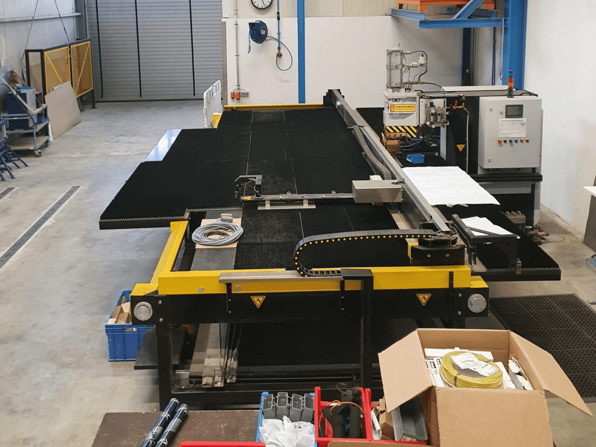 Rūpnieciskā griešanas iekārta ar dzelteniem un melniem elementiem, skats no priekšpuses, kurā redzamas vadības ierīces un piederumi rūpnīcas apstākļos.