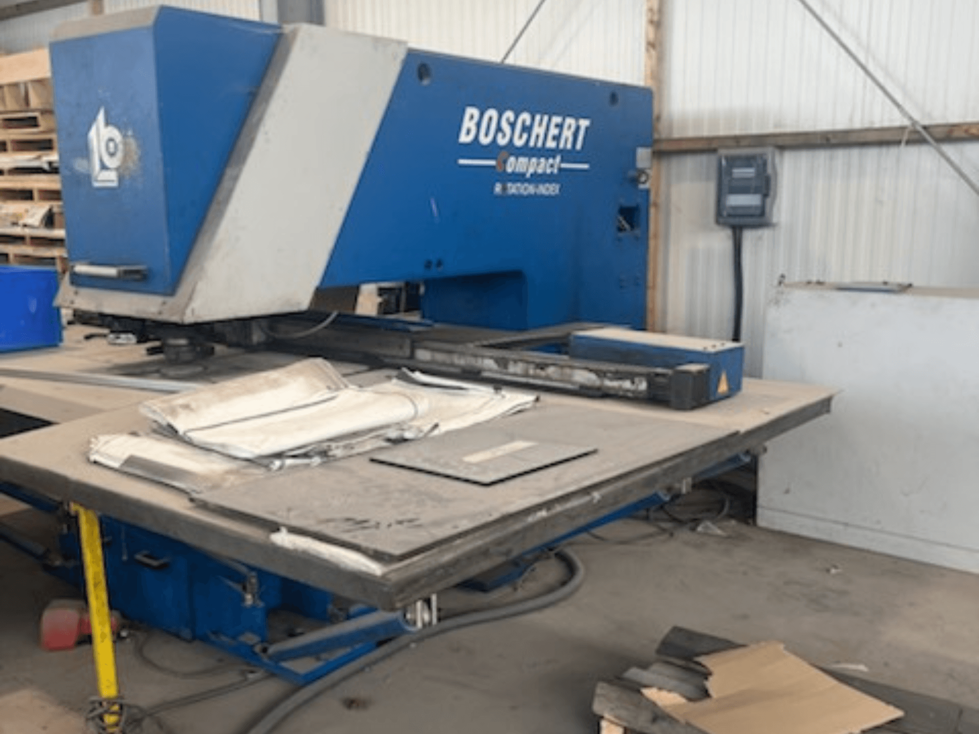 BOSCHERT COMPACT 1000 CNC perforācijas mašīna darbnīcā, redzams priekšskats ar metāla loksnēm uz galda.