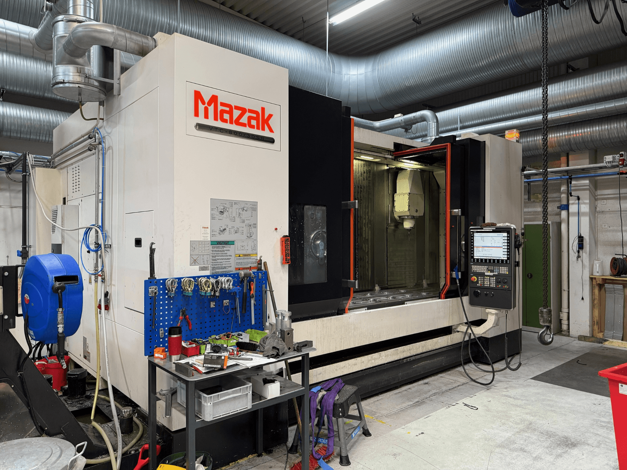 Mazak CNC darbagalds no priekšpuses, kurā redzamas vadības ierīces, darbarīki un darba vieta apstrādes vidē.