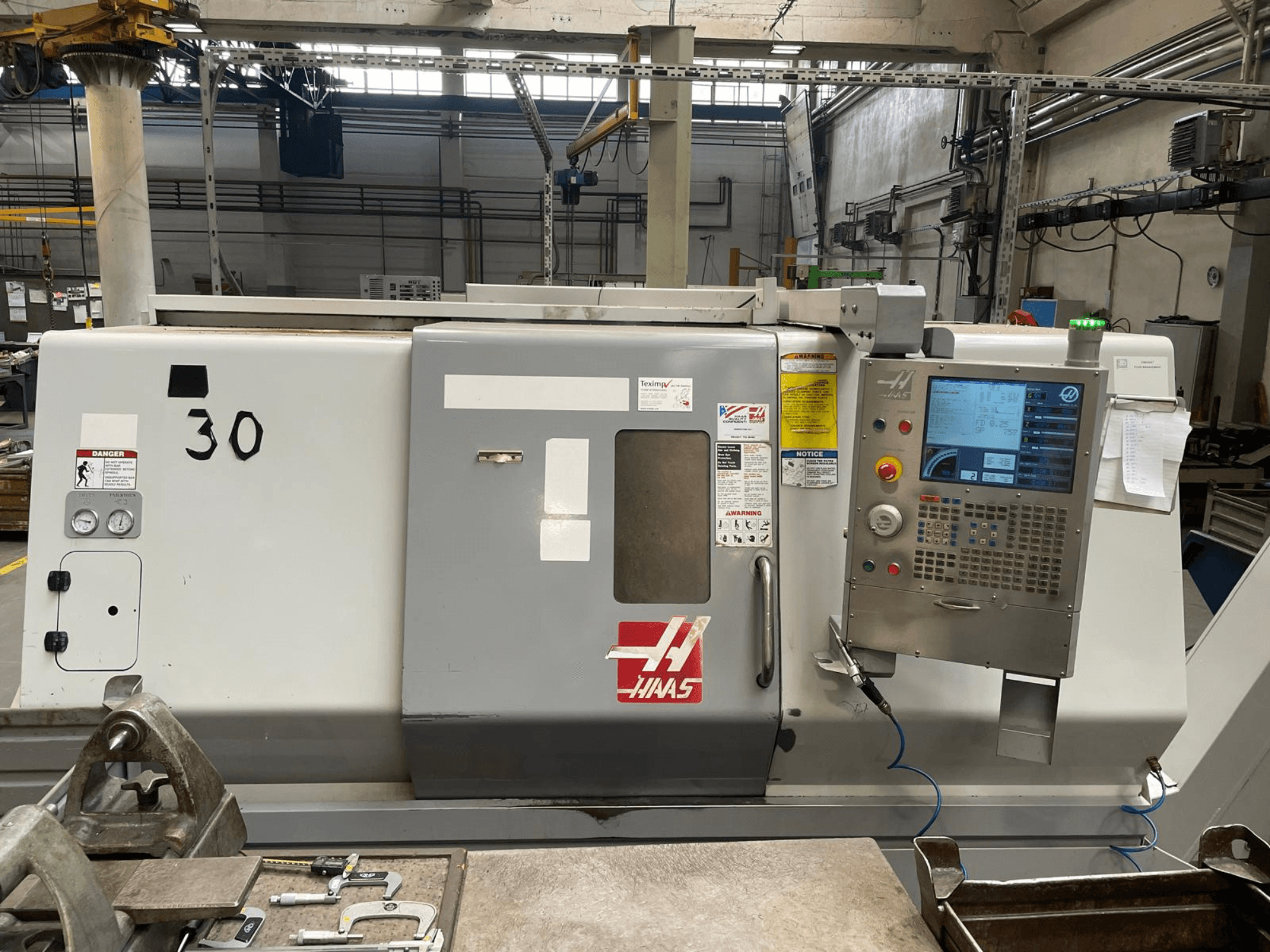 Haas SL-30THE horizontālās virpošanas mašīnas skats no priekšpuses, kurā redzams digitālais vadības panelis, brīdinājuma uzlīmes un modeļa numurs 30.