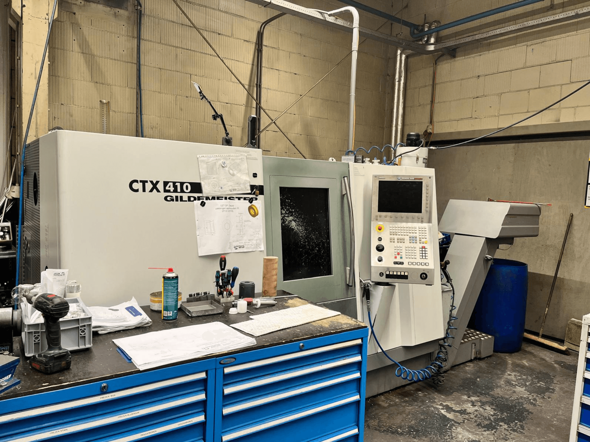 Gildemeister CTX 410 CNC darbnīcā, skats no priekšpuses, ar vadības paneli un dažādiem instrumentiem uz darbgalda.