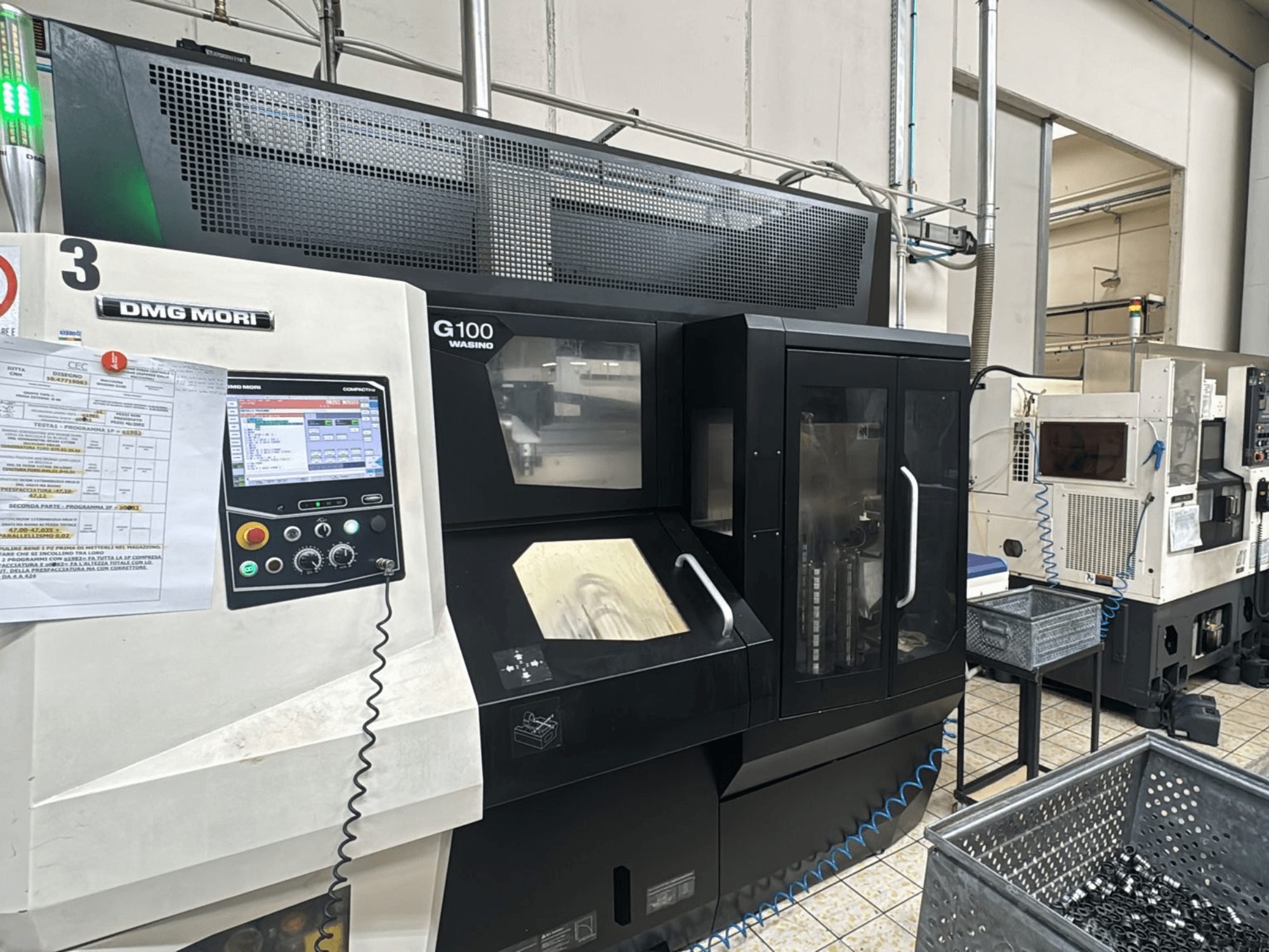 DMG MORI G100 mašīna rūpnīcā, skats no priekšpuses, ar digitālo vadības paneli un blakus esošajām instrumentu glabāšanas kastēm.