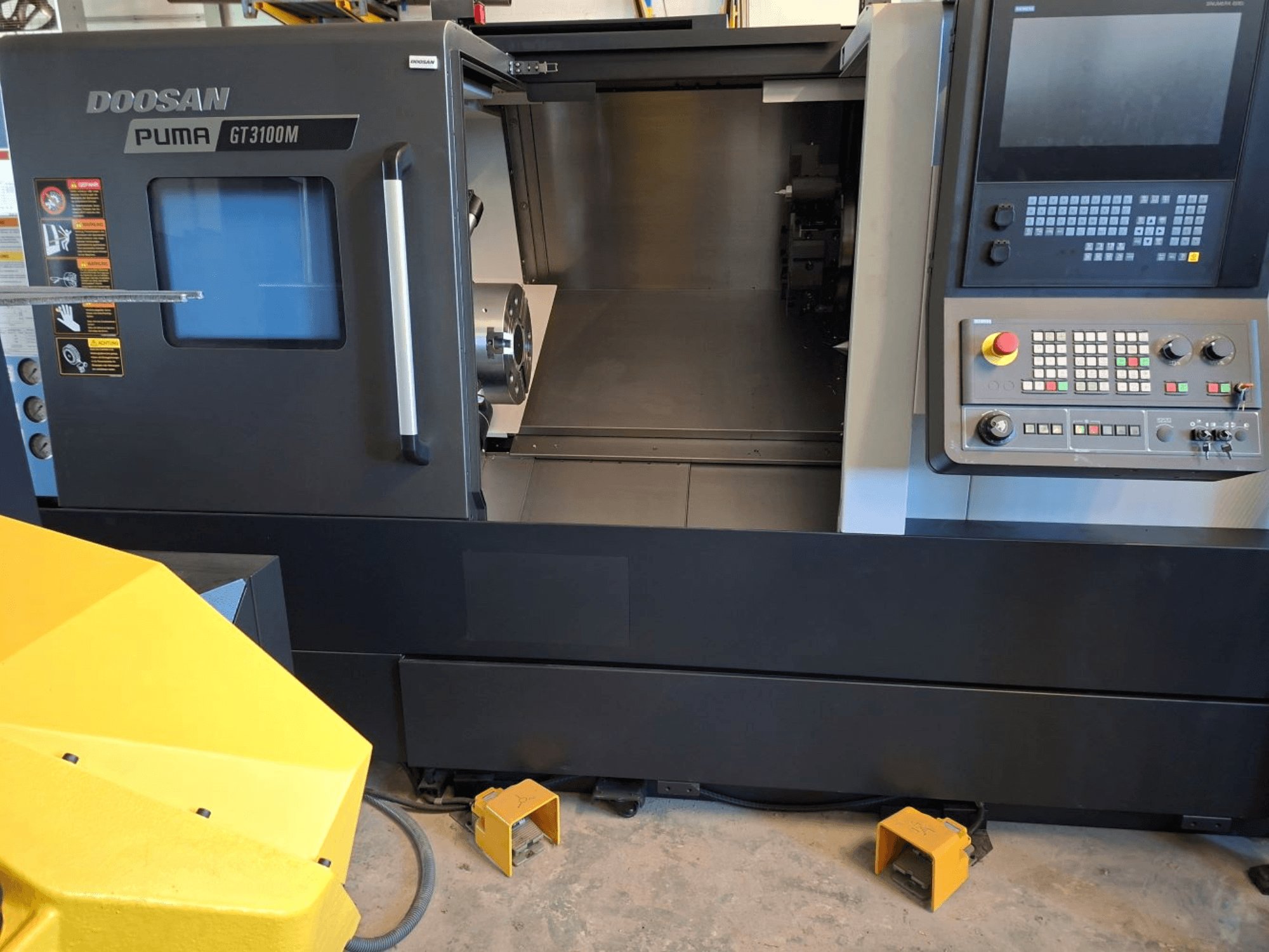 DOOSAN Puma GT 3100 M horizontālās virpošanas darbgalds priekšpusē, kurā redzams vadības panelis, atvērtais tornis un iekšējā darba telpa.