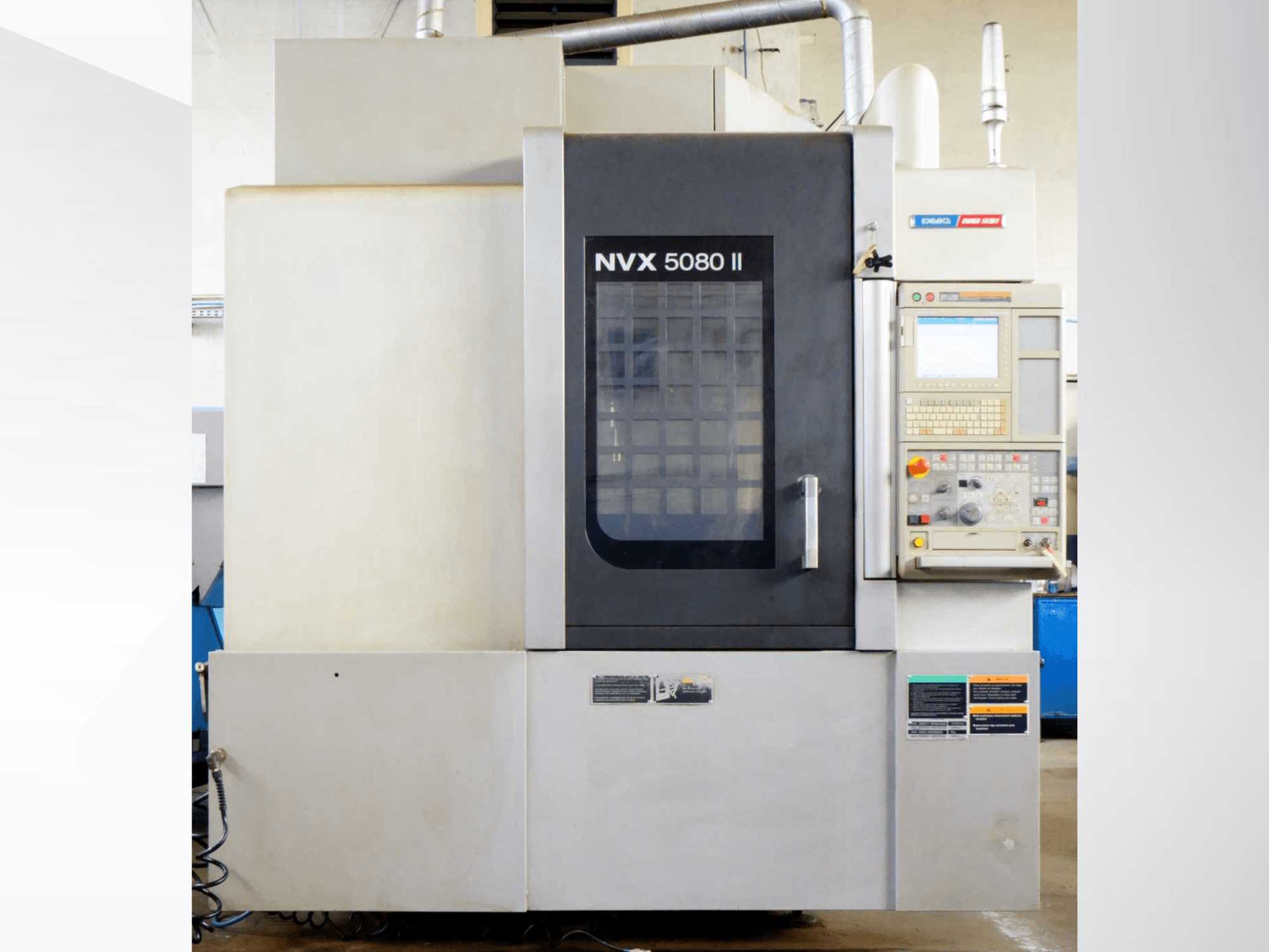 Vertikālais apstrādes centrs DMG Mori Seiki NVX 5080 II, skats no priekšpuses, kurā redzams vadības panelis un režģu durvju konstrukcija.