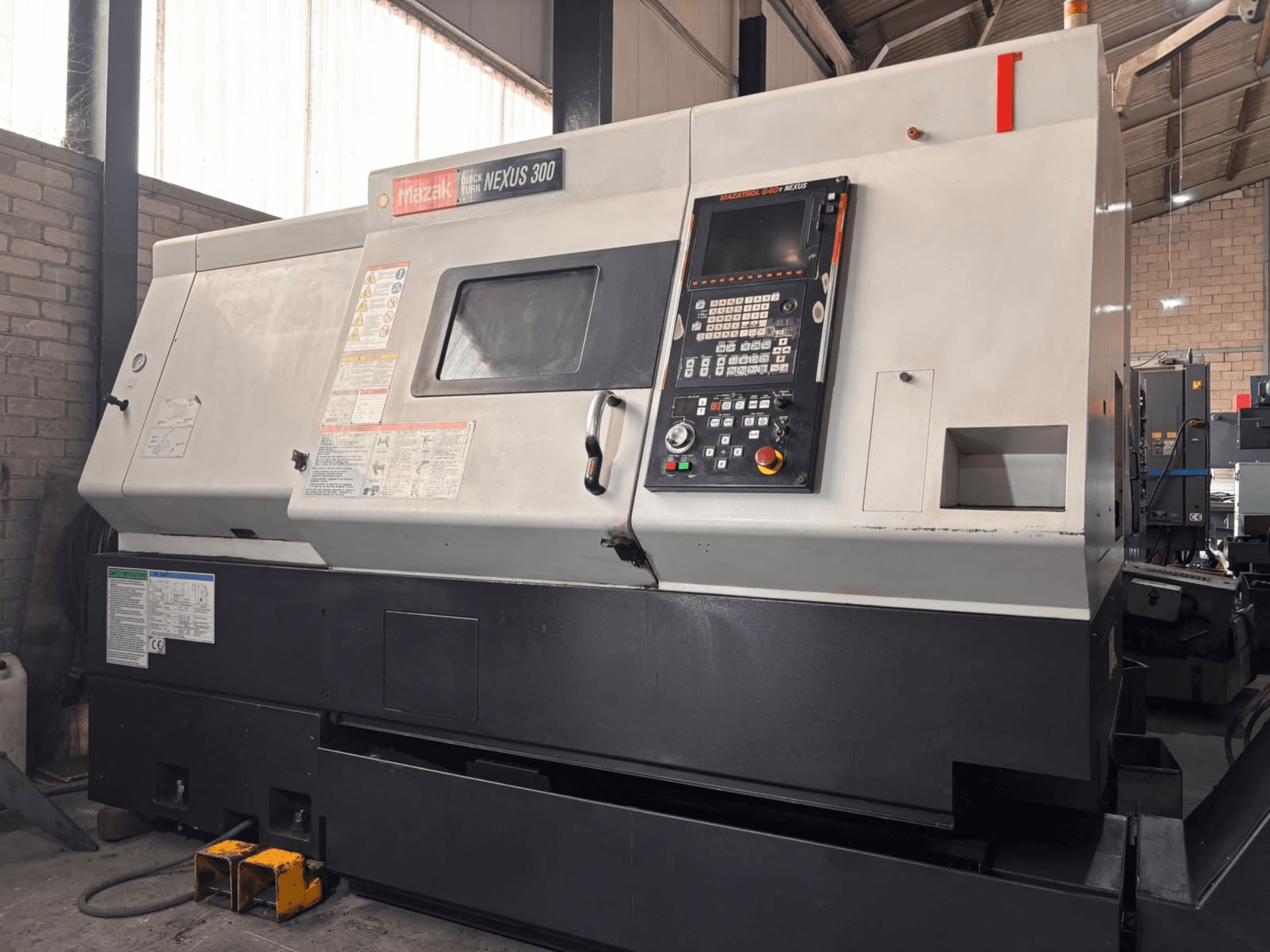 Mazak QT NEXUS 300 horizontālā virpošanas mašīna, sānskats, kurā redzams vadības panelis un darbības indikatori darbnīcas vidē.