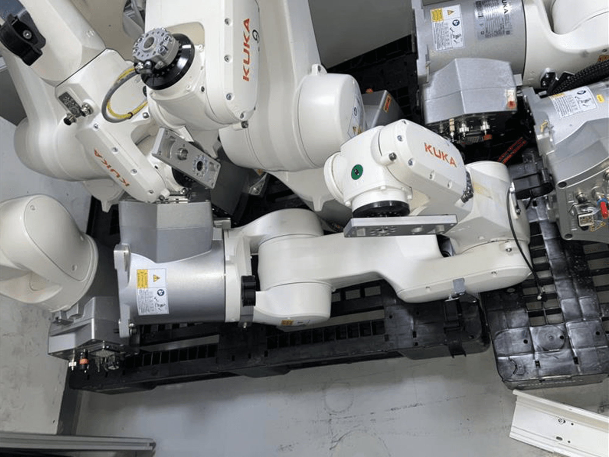 KUKA KR 6 R900 CR robota roka no augšas, ar vairākām locītavām un motoriem, uzstādīta uz melnas pamatnes ar kabeļiem.