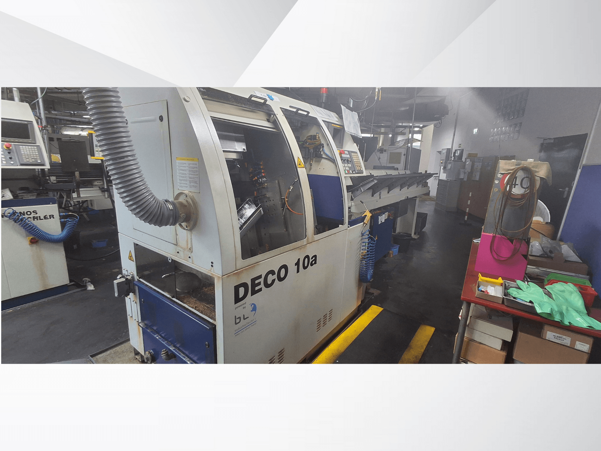 DECO 10a CNC darbnīcā, skats no priekšpuses; vadības panelis un putekļu nosūces sistēma, blakus darbgalds.