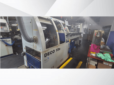 DECO 10a CNC darbnīcā, skats no priekšpuses; vadības panelis un putekļu nosūces sistēma, blakus darbgalds.