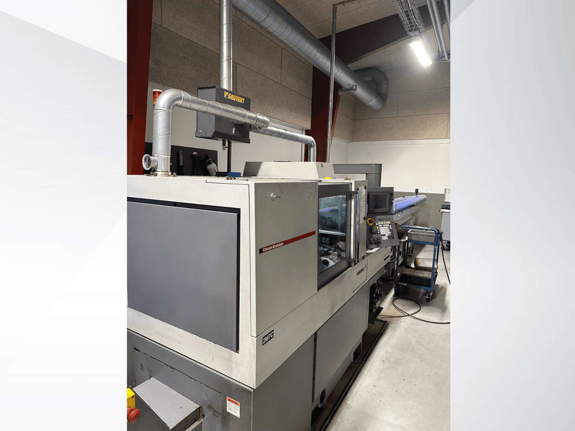 MVC zīmola rūpnieciskās iekārtas, skats no sāniem, redzams vadības panelis un cauruļvadi, uzstādītas rūpnīcas vidē.