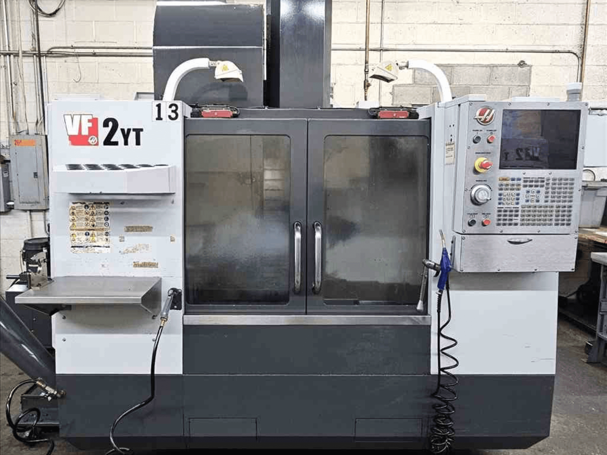 HAAS VF-2YT vertikālā apstrādes centra priekšējais skats, kurā redzams vadības panelis un stikla durvis.
