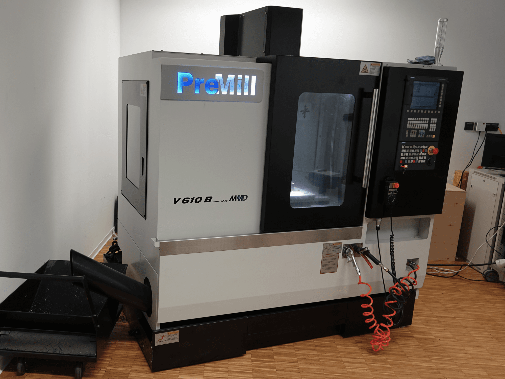 Vertikālais apstrādes centrs „PreMill V 610 B“, skats no priekšpuses, kurā redzams vadības panelis, dzesēšanas šķidruma sistēma un pievienotās gaisa šļūtenes.