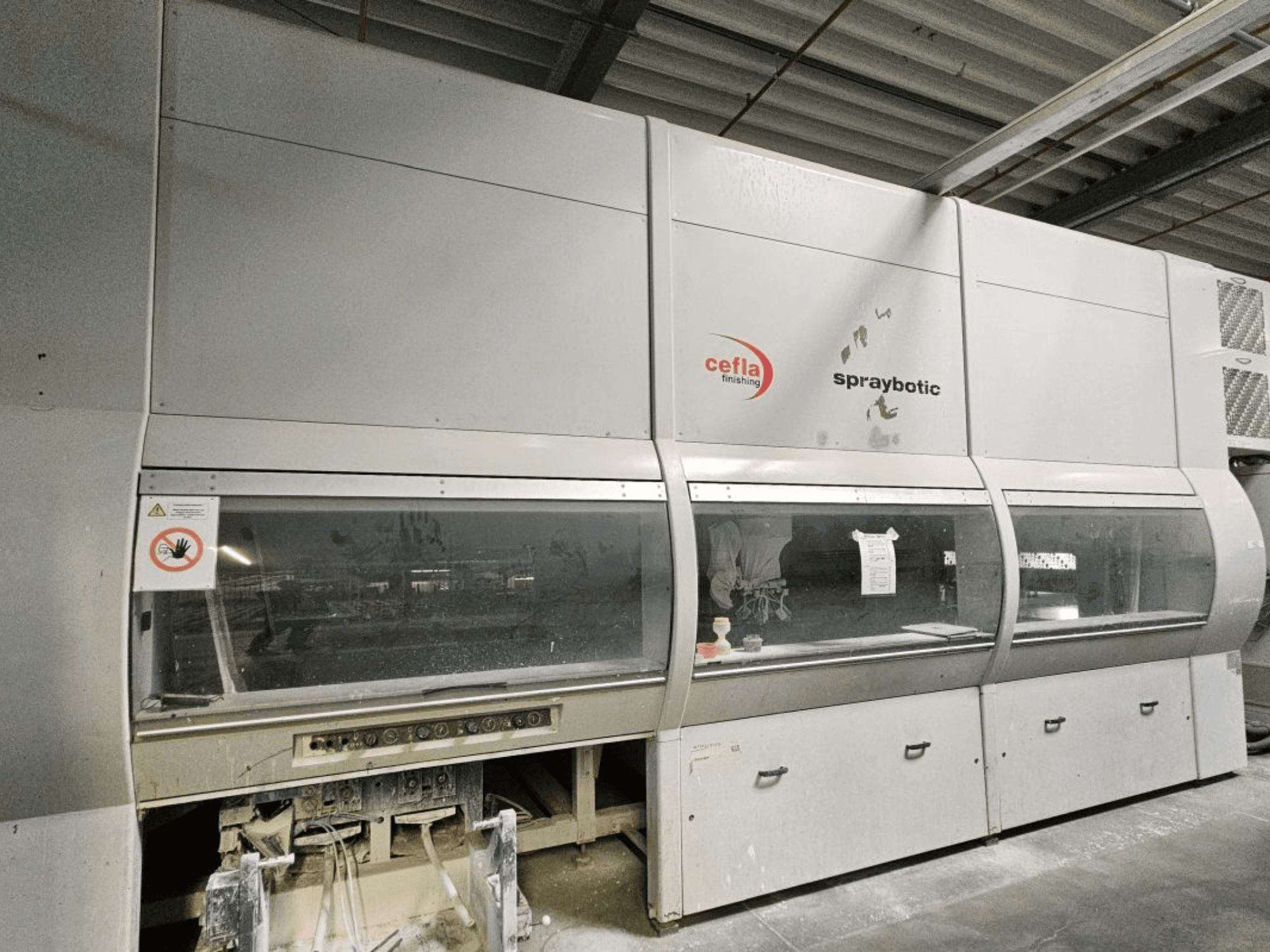 Cefla Spraybotic MD ražošanas līnija kokam, skats no priekšpuses, kurā redzams vadības panelis un caurspīdīgi logi.
