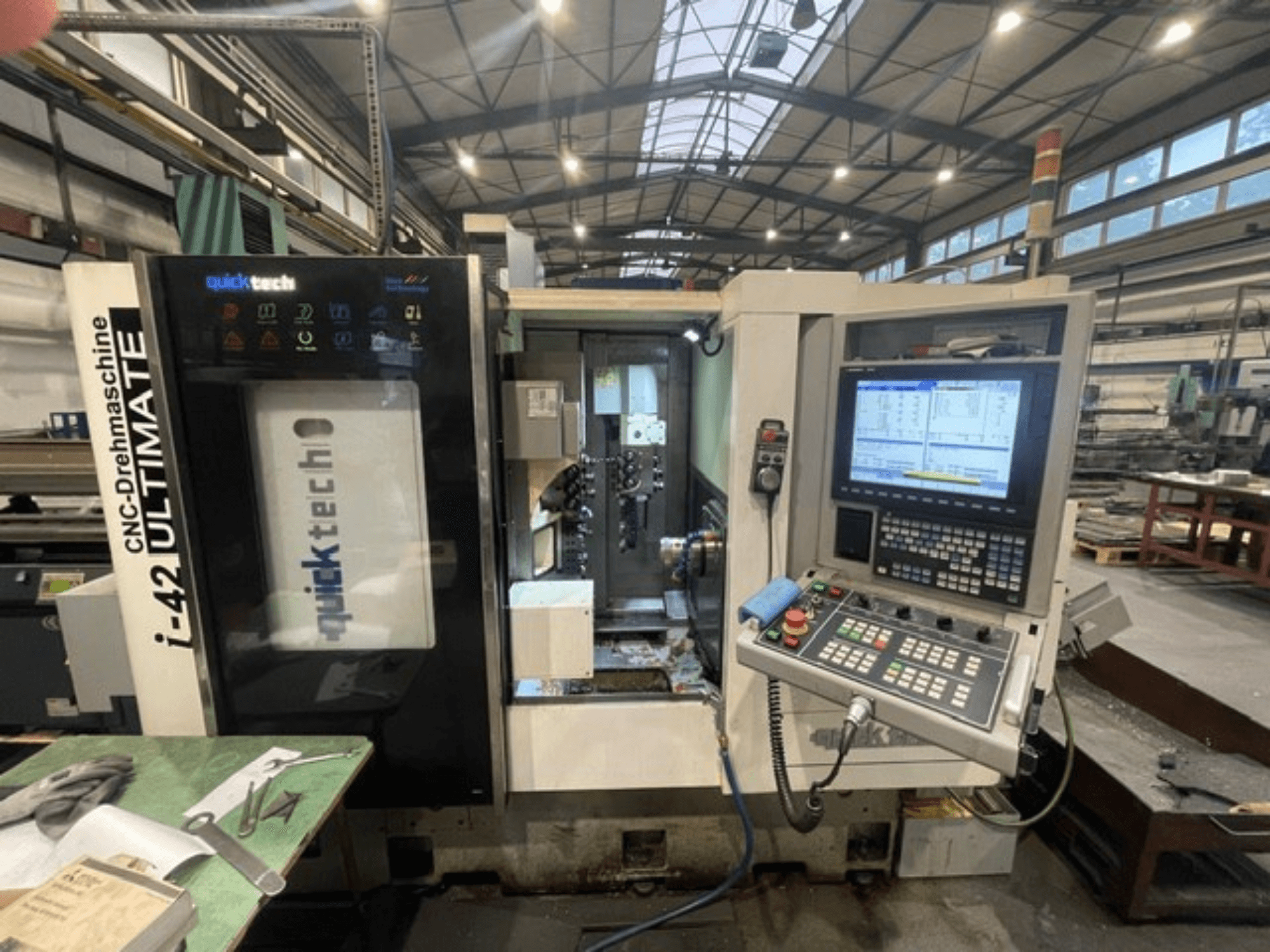 Quick-Tech I-42U Šveices tipa virpošanas mašīna, priekšējais skats, kurā redzams vadības panelis un CNC saskarne darbnīcā.